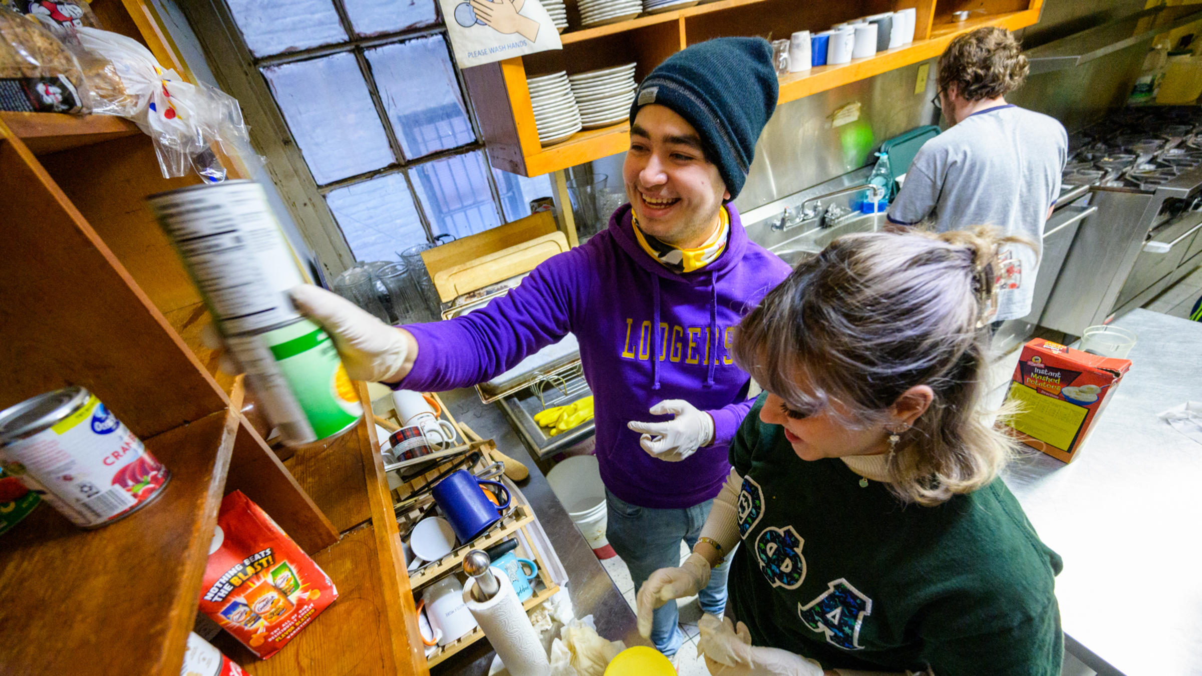 People putting cans of food into a kitchen cabinet