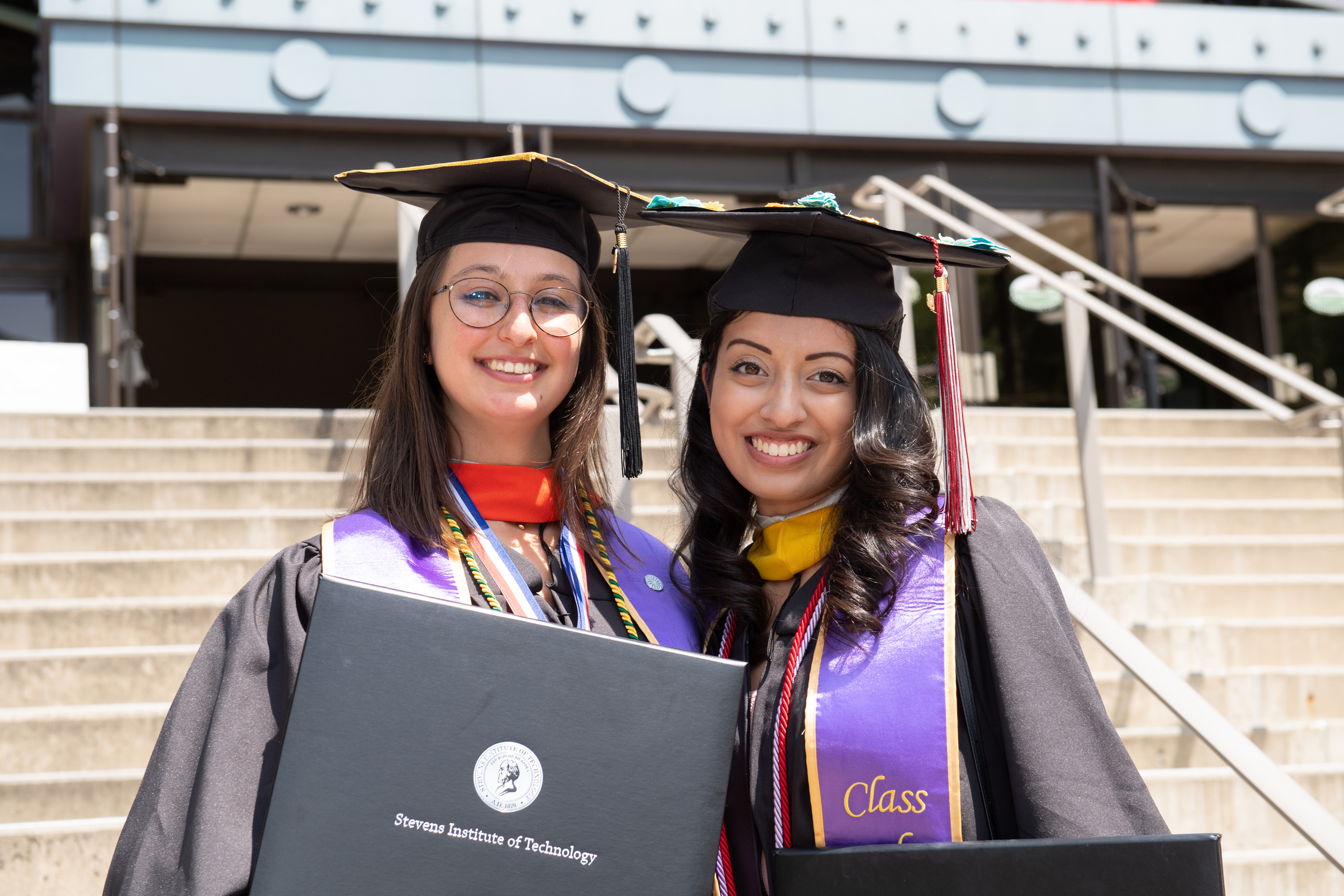 Two women graduates dressed in regalia showing off their degrees