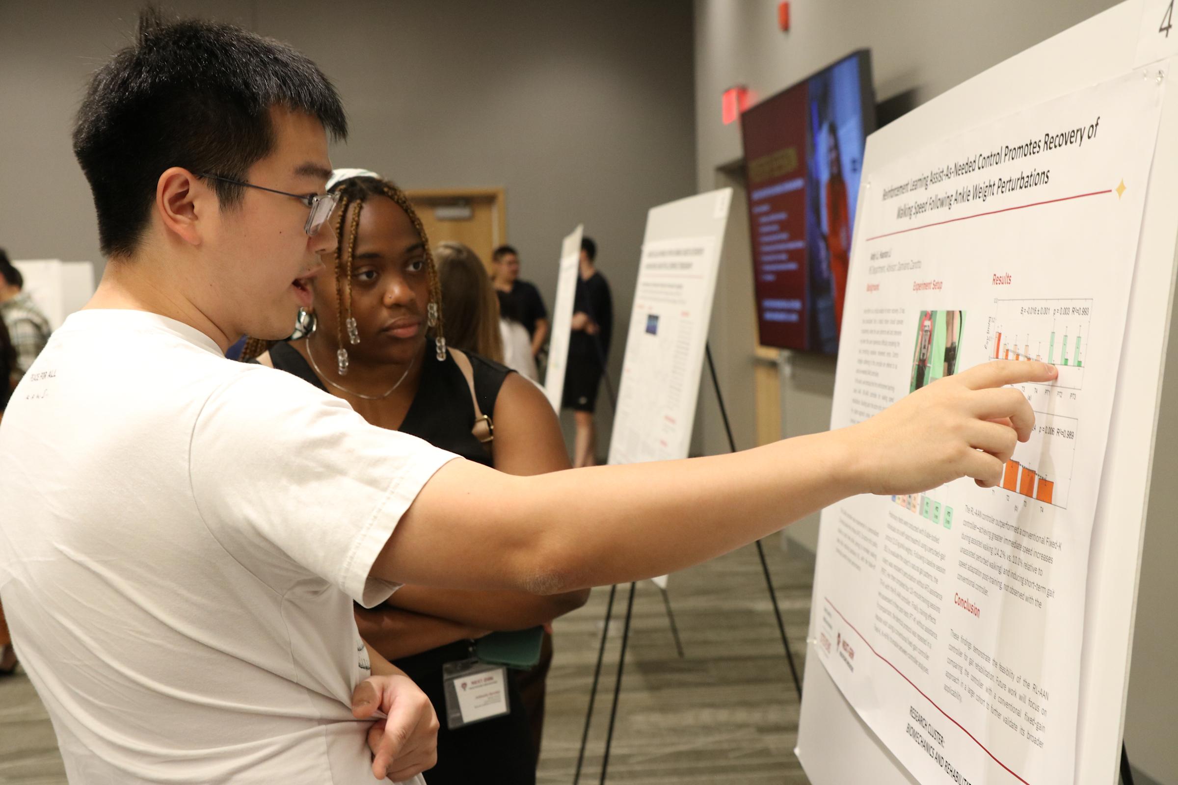 Two students pointing and examining a presentation board.