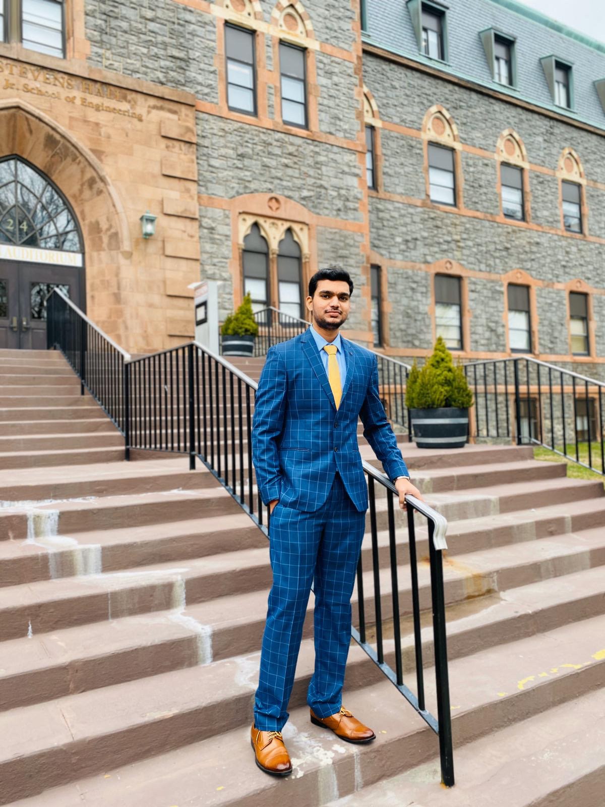 Vinoth Kolluru M.S. ’21 stands in a suit in front of the EAS building at Stevens Institute of Technology's campus