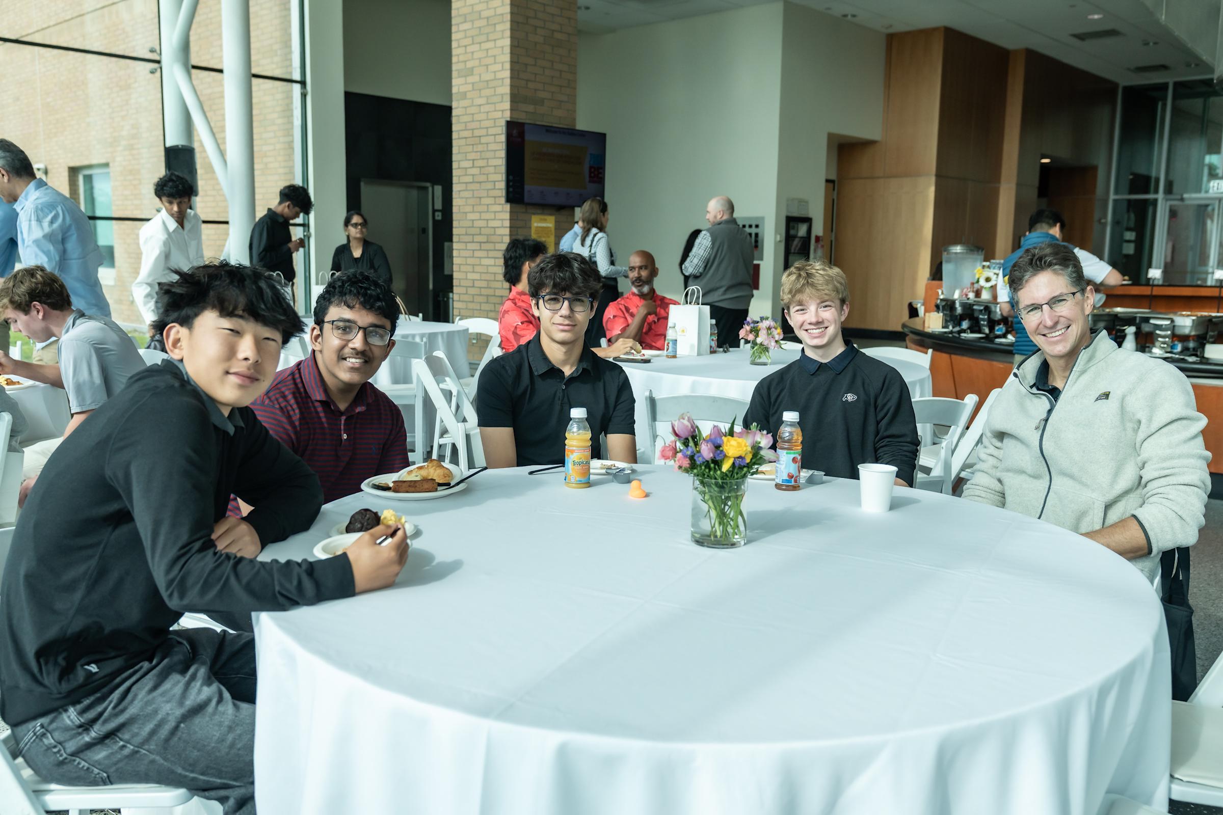 Students and families sit around a round table during breakfast in the Babbio Center atrium.