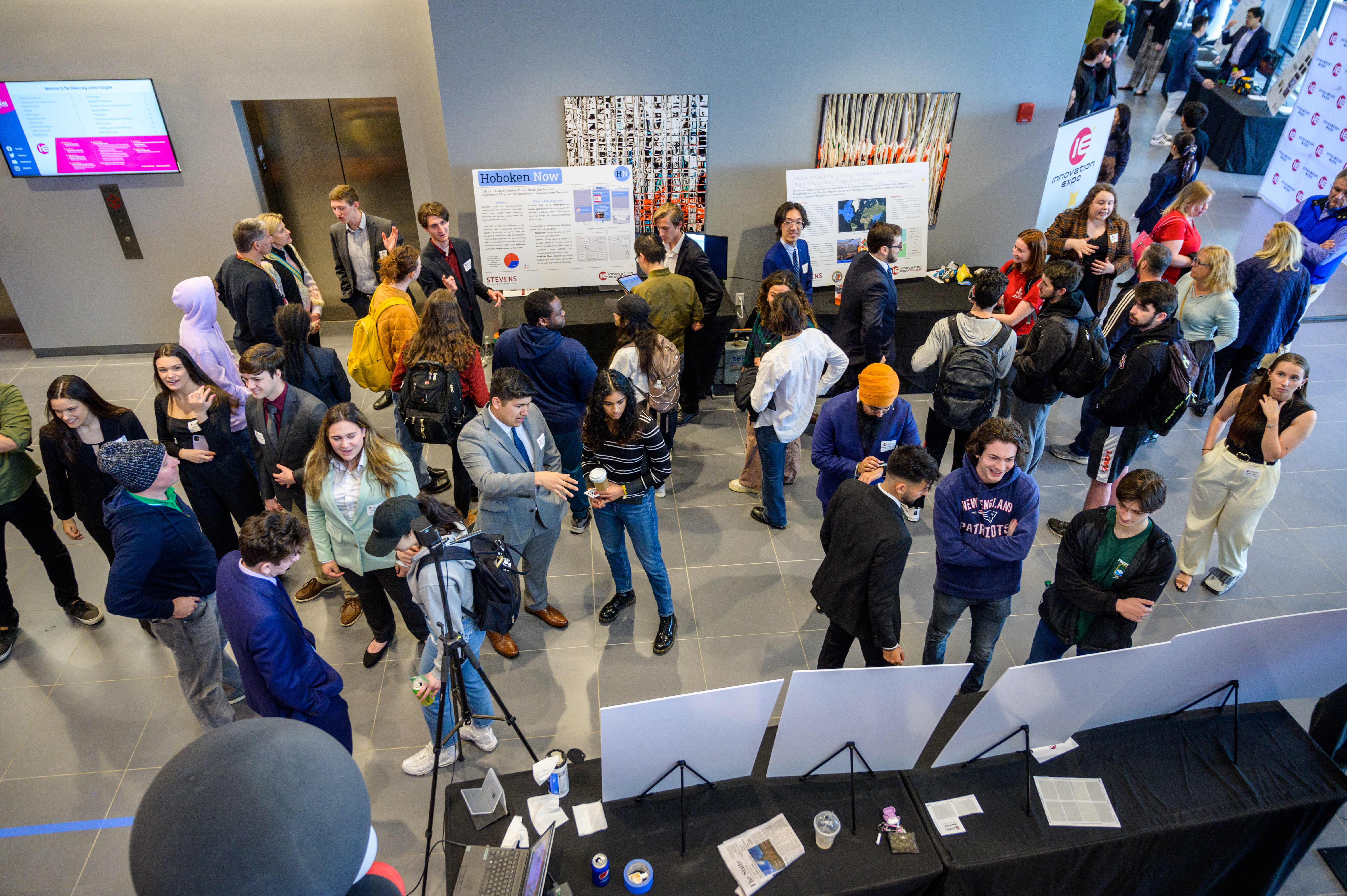 An overhead shot of students and faculty browsing project posters and presentations in the lobby of the UCC. 