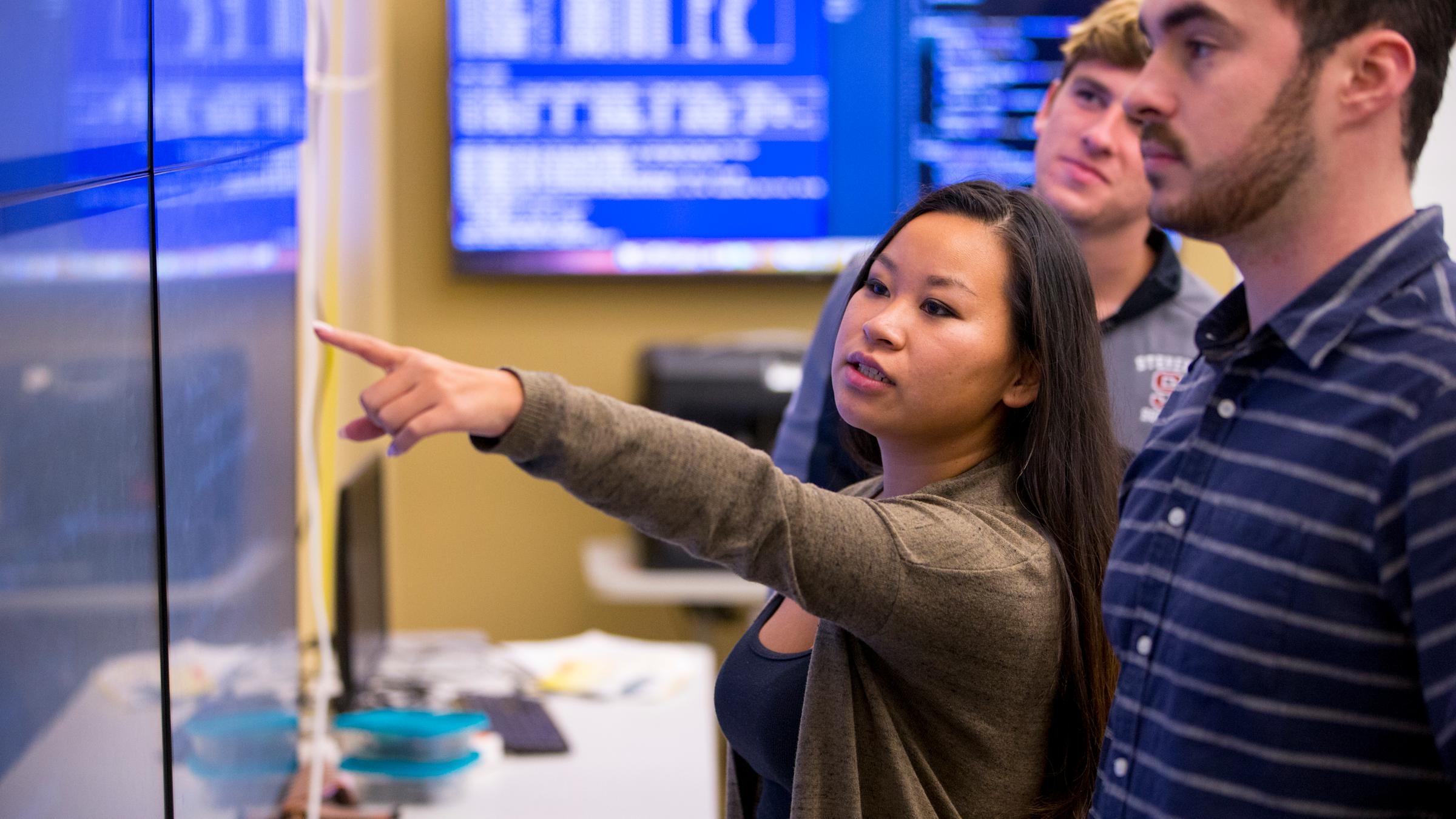 Students standing in class analyzing code on wall screen
