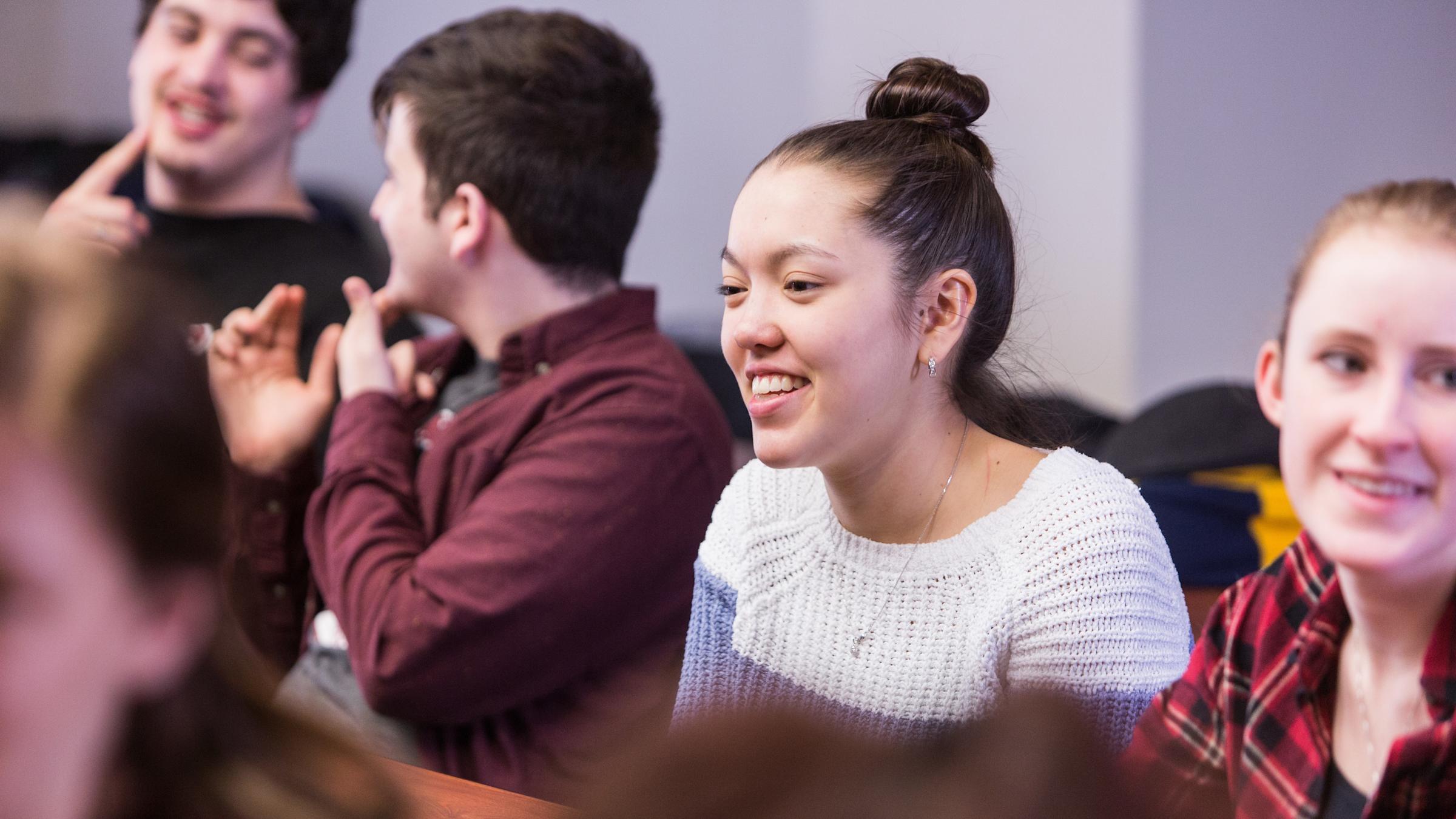 Female student smiling in a classroom surrounded by male and female colleagues