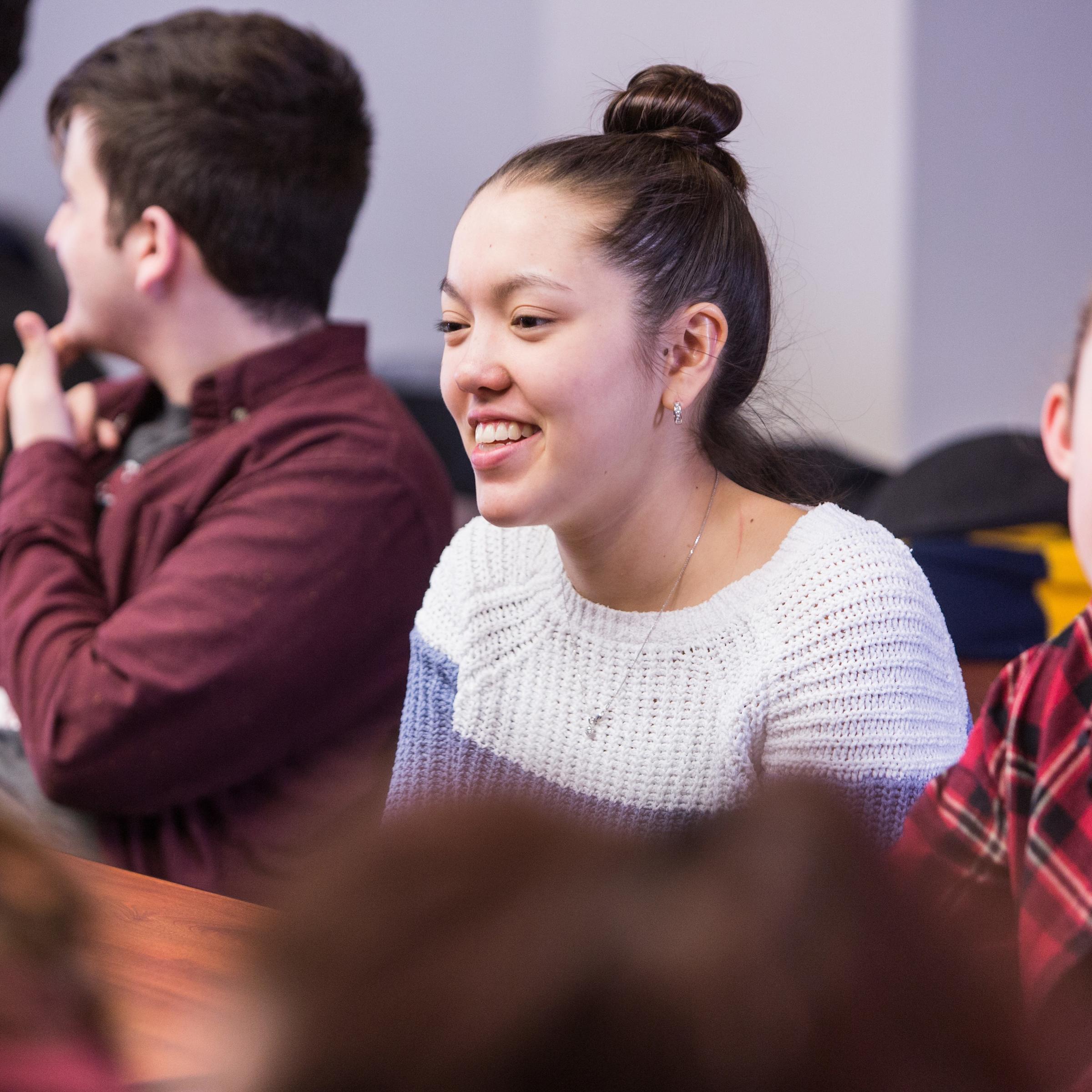 Female student smiling in a classroom surrounded by male and female colleagues