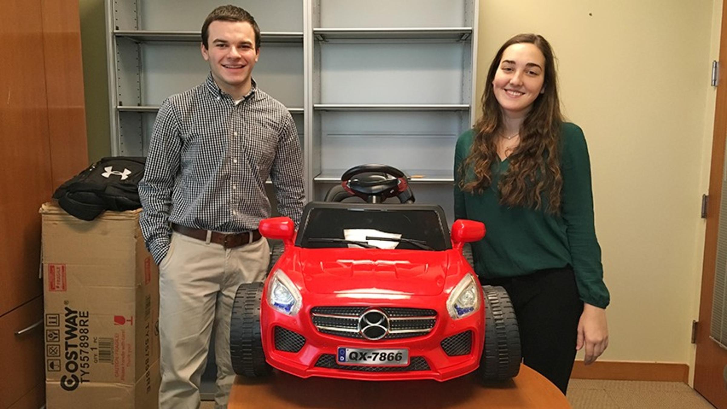 A male and female student in a Stevens office, standing with a red toy car they rewired for students with disabilities.