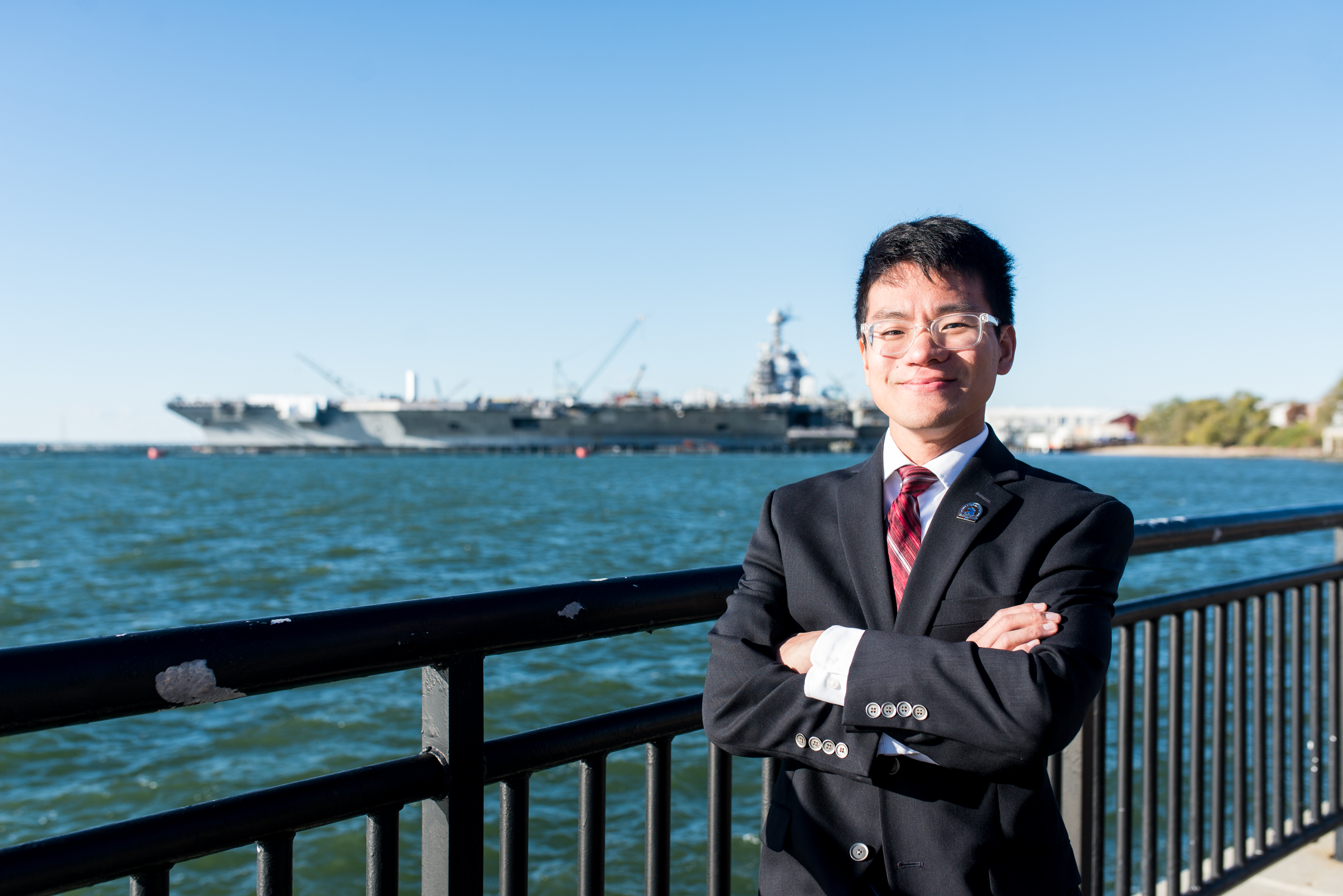 Haijun Ramoundos smiling for the camera in front of Newport News Shipbuilding dock.