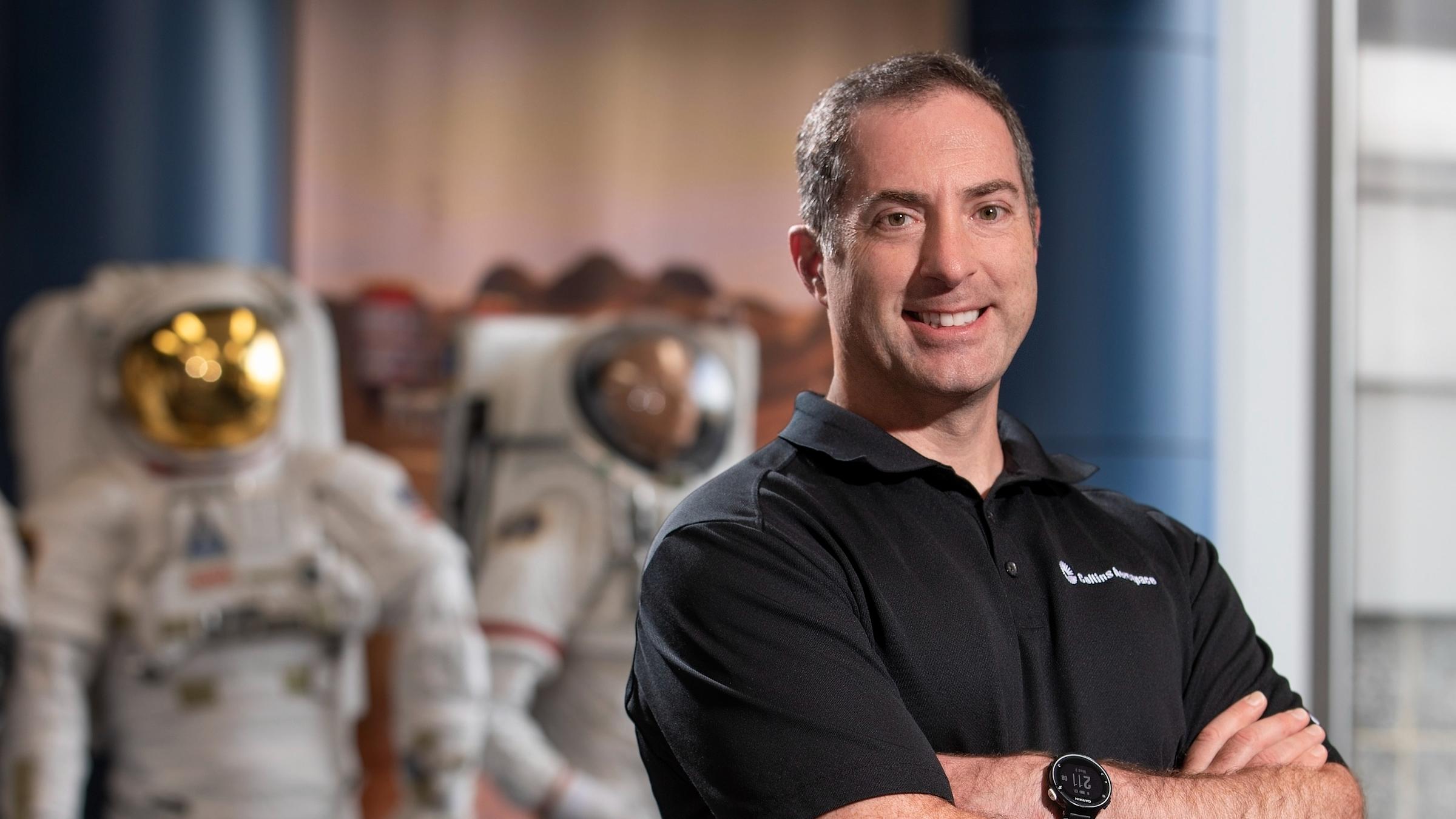 Greg Quinn ’00 stands with spacesuit displays at Collins Aerospace.