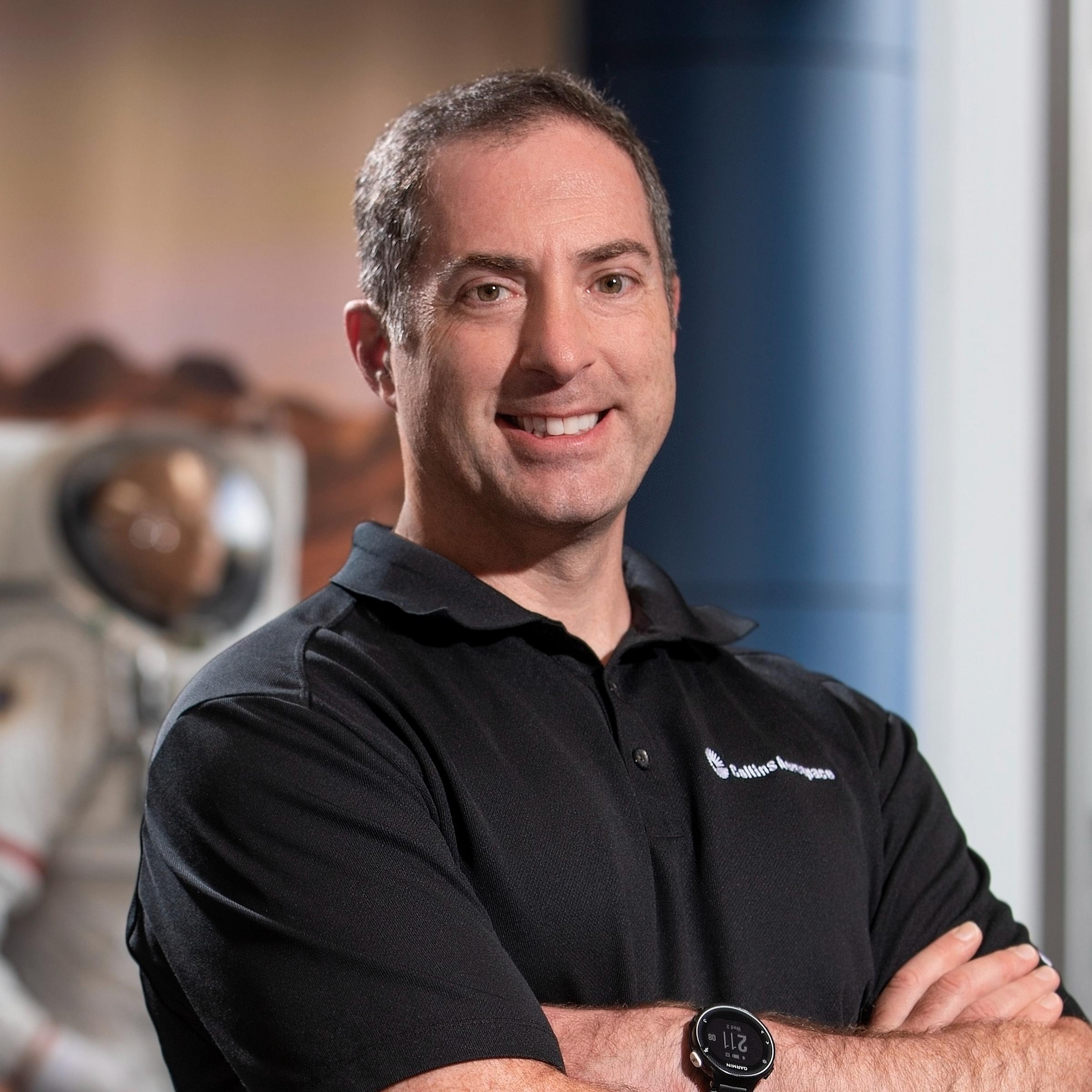 Greg Quinn ’00 stands with spacesuit displays at Collins Aerospace.