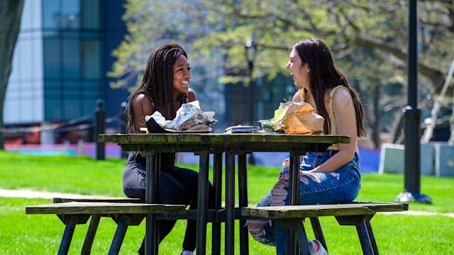 Two female students laugh outside on picnic table