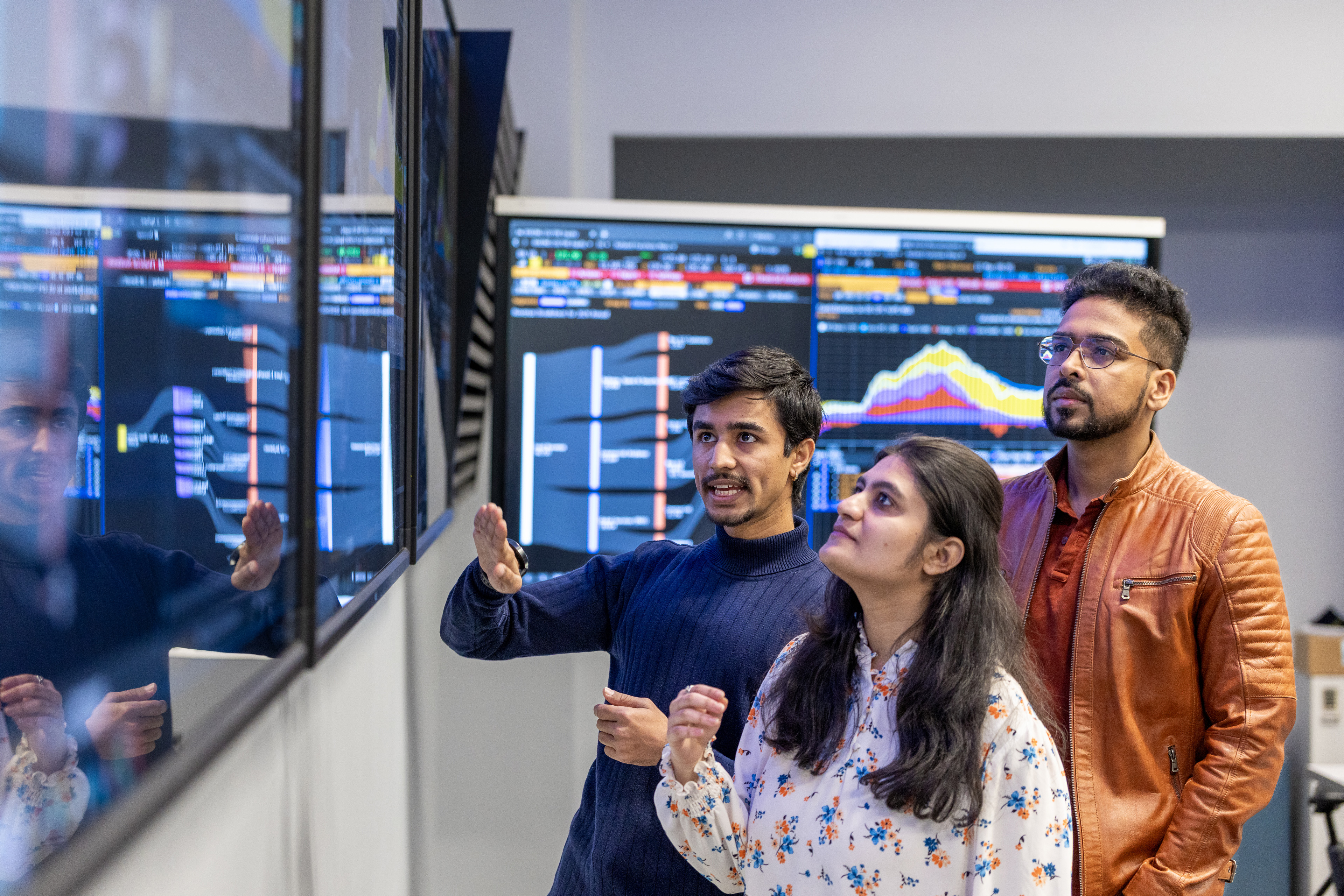 Three students discuss data displayed on a large screen in front of them. 