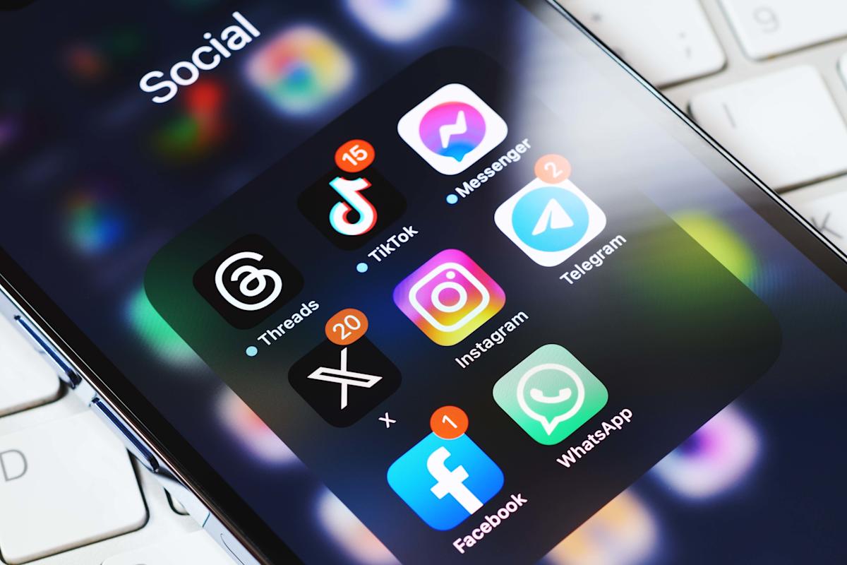 Phone displays multiple social media icons with a laptop in the background.