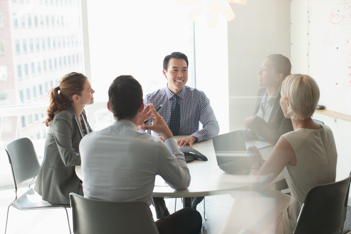 one man smiling with group of coworkers around a conference table