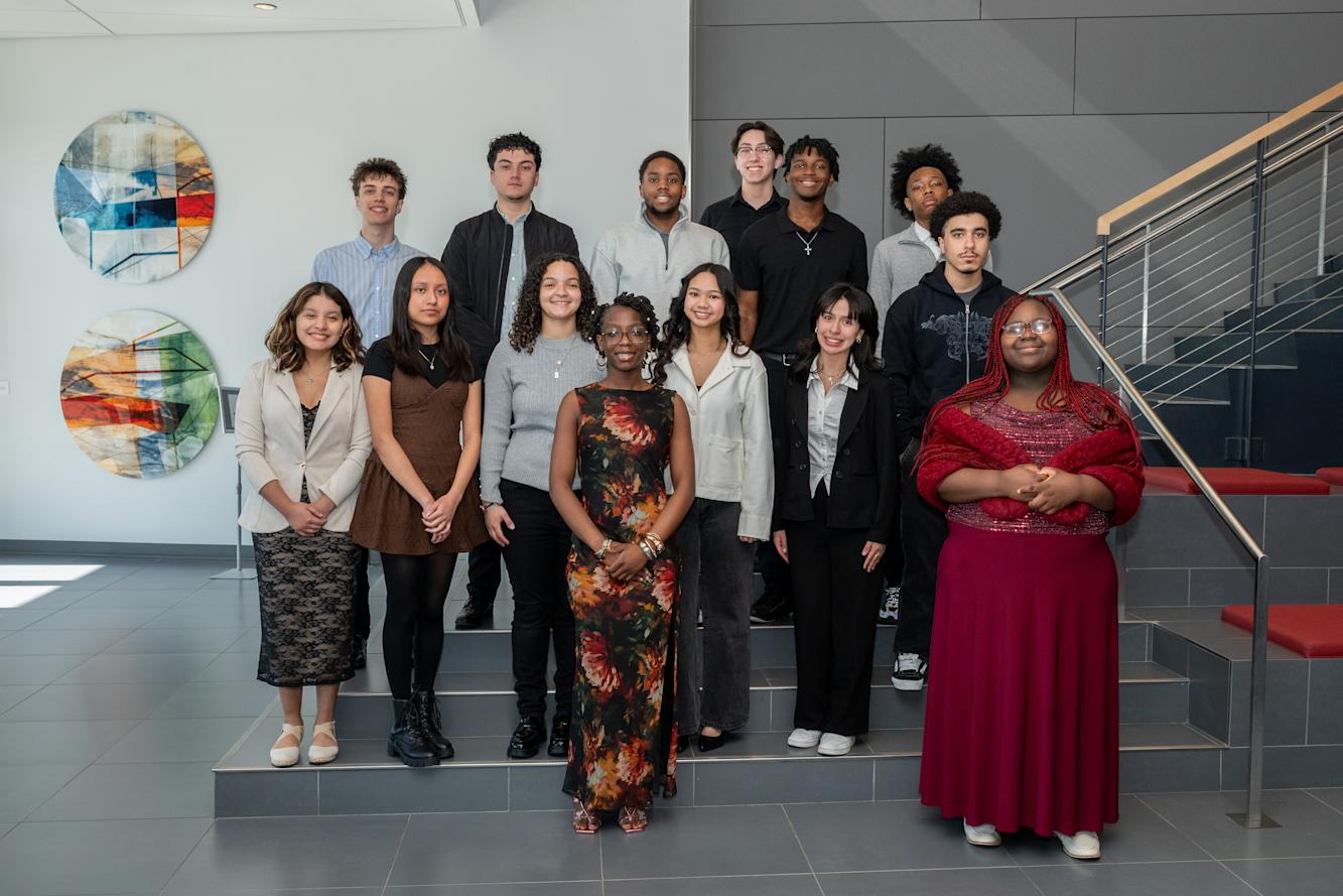 A group of high school students--both male and female and different races and ethnicities--stand in front of a staircase.