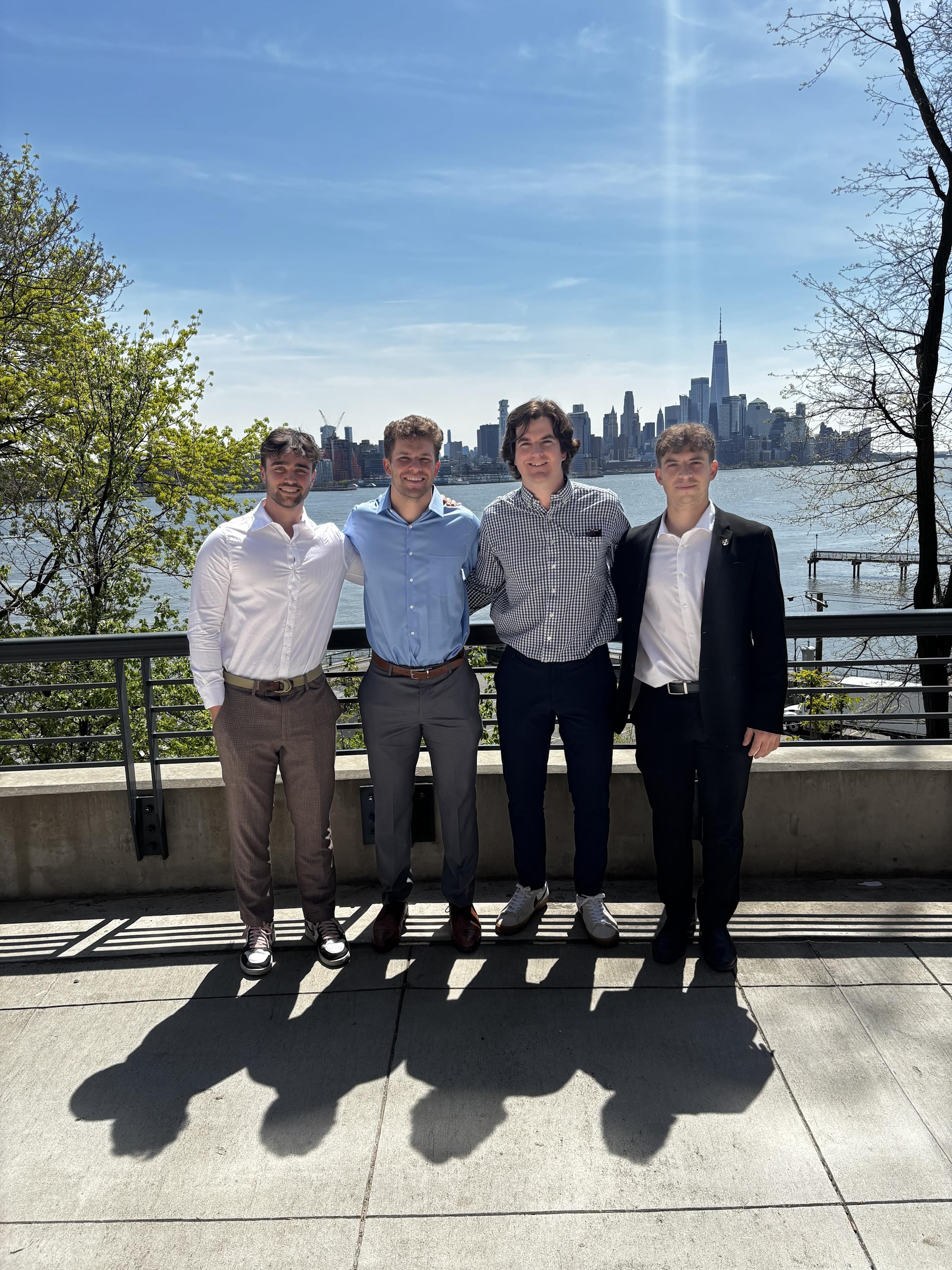 A group of 4 sudents stand in front of the Hudson River with the view of the New York City skyline in the background.