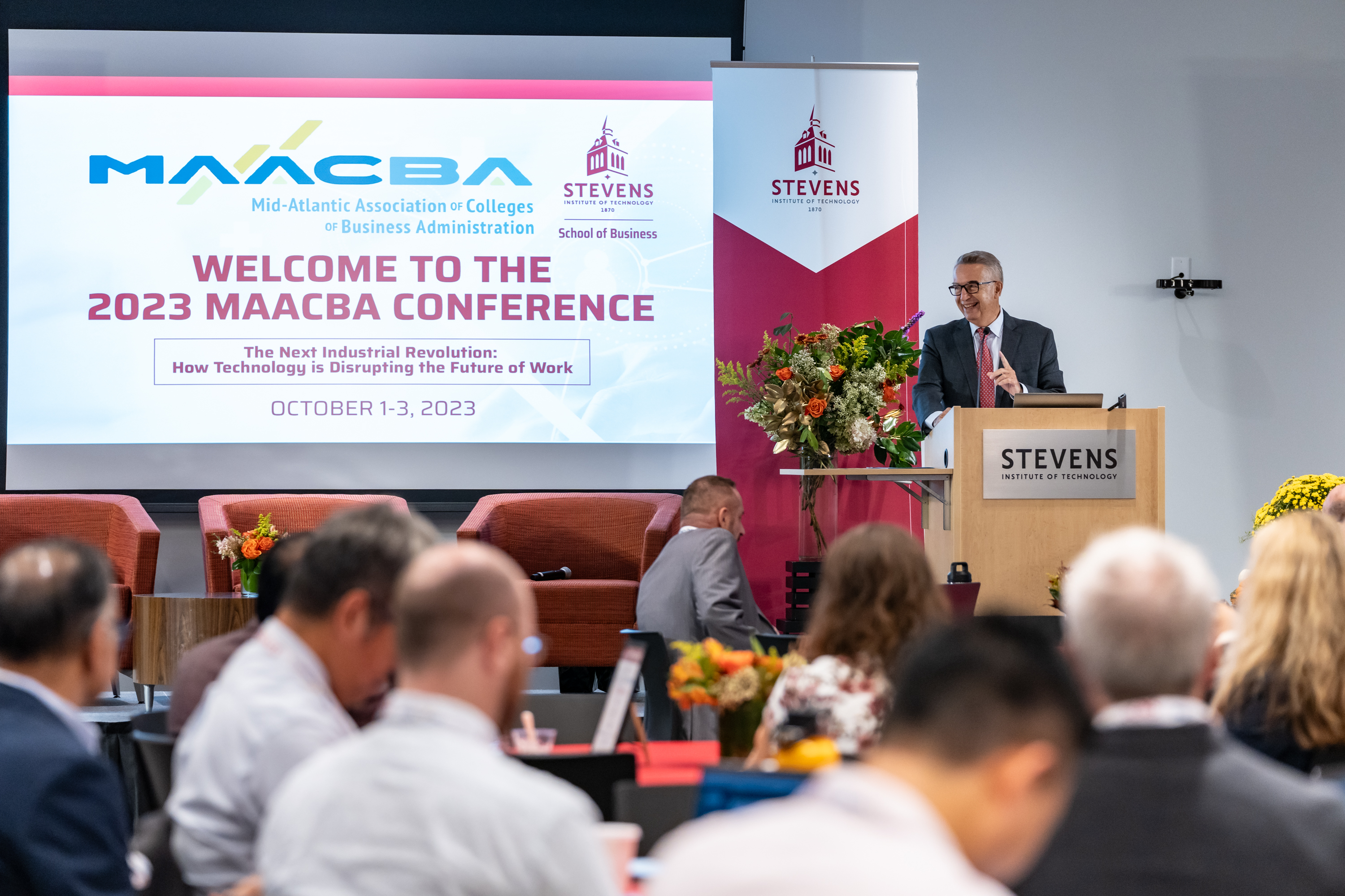 Dean Gregory Prastacos stands in front of a podium addressing the audience at the 2023 MAACBA Conference.