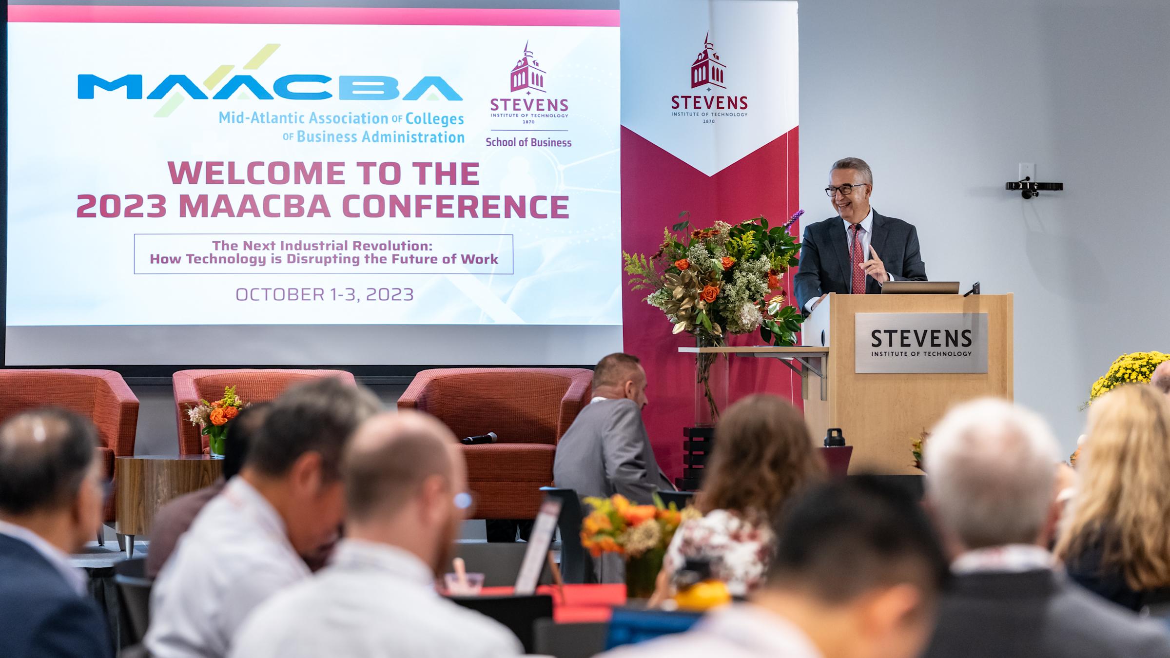 Dean Gregory Prastacos stands in front of a podium addressing the audience at the 2023 MAACBA Conference.