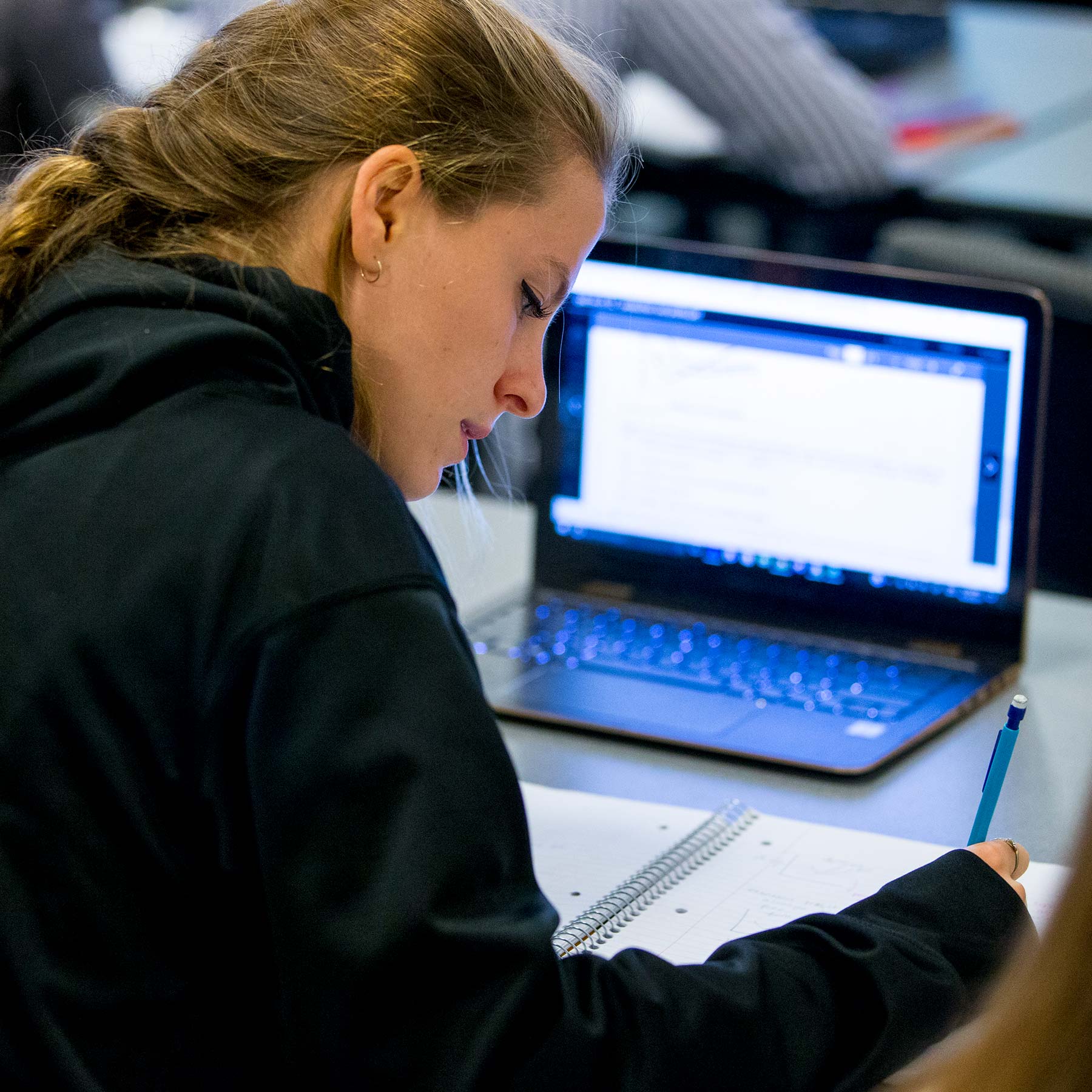 A female student writing and working on a laptop.