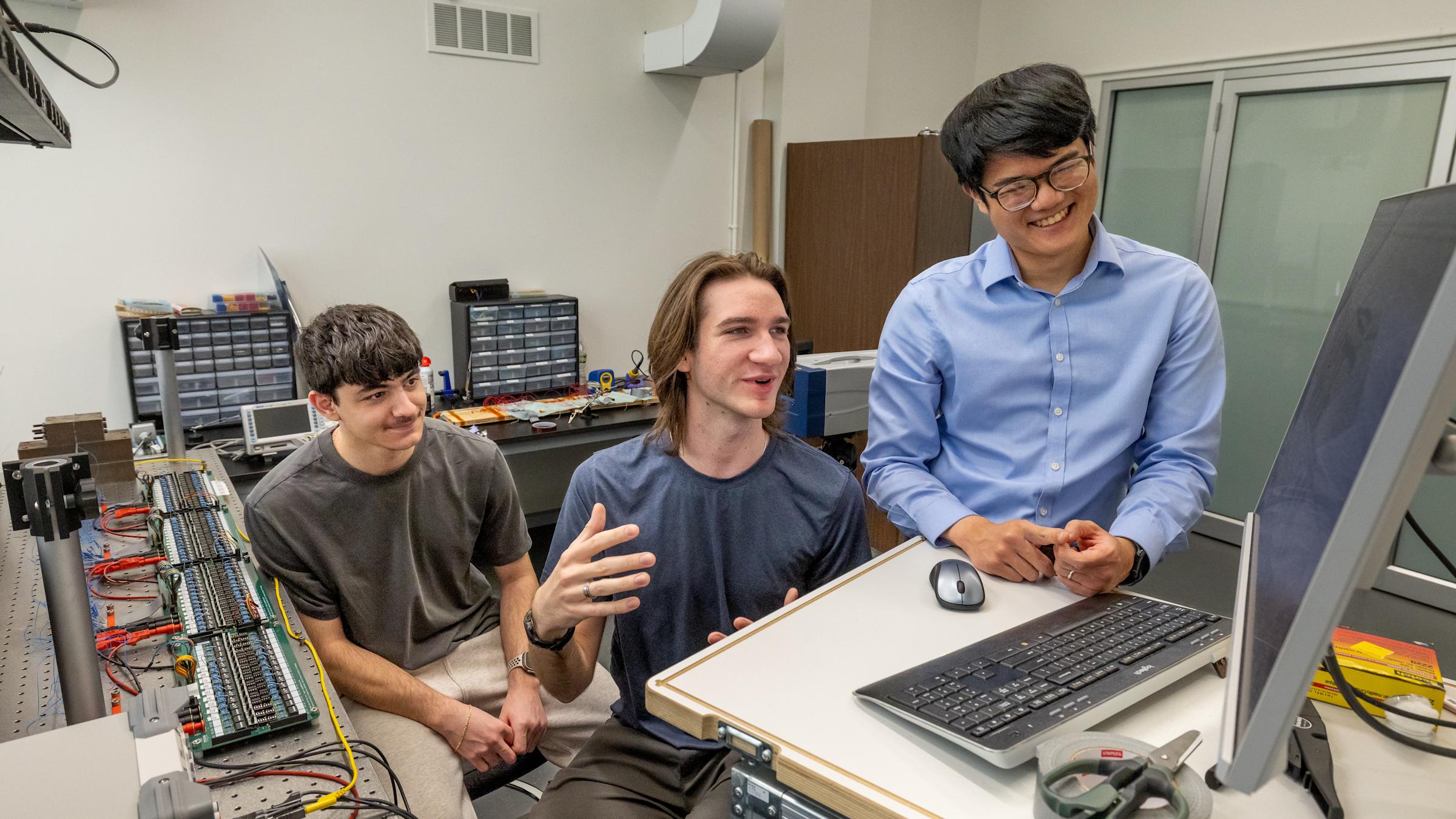 Two students and professor Christopher Sugino looking at a monitor in a mechanical engineering department lab.