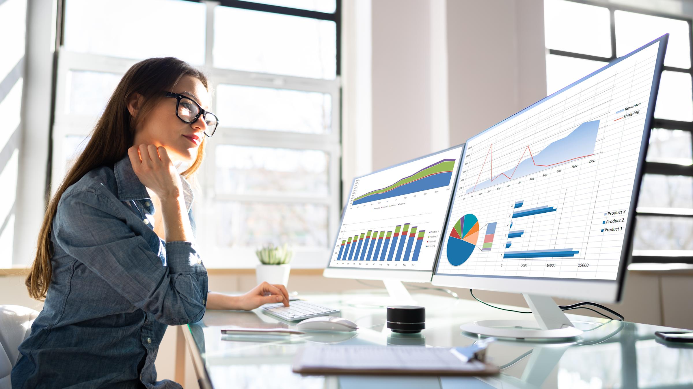 woman looking at charts on two computer screens