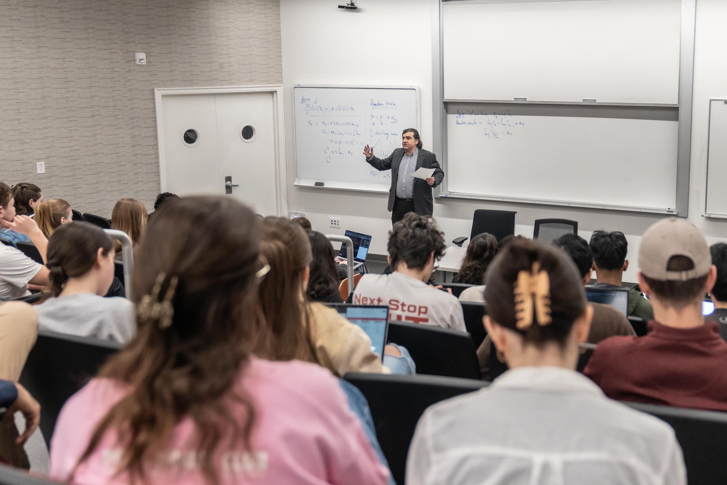 Ionut Florescu teaches from the front of the classroom with students looking on and whiteboards in the background.