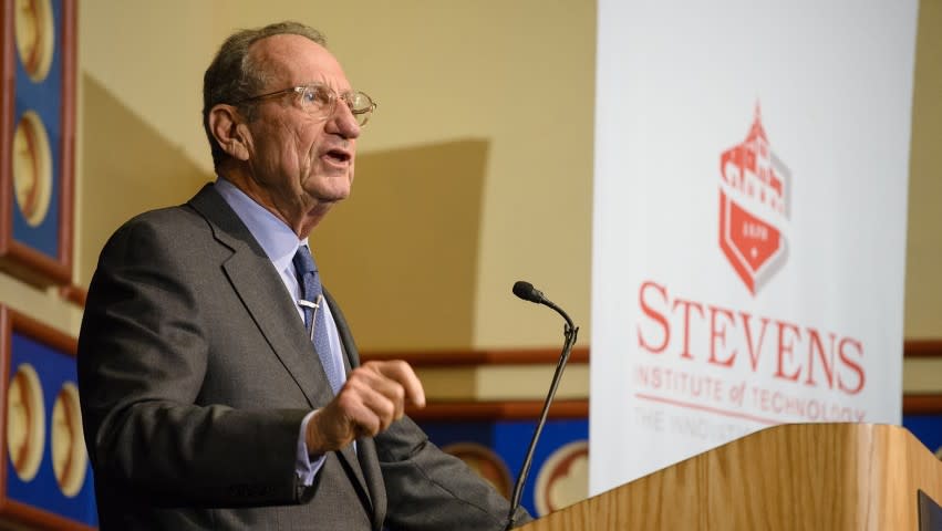 Dr. John Deutch giving a speech behind a podium at Stevens Institute of Technology