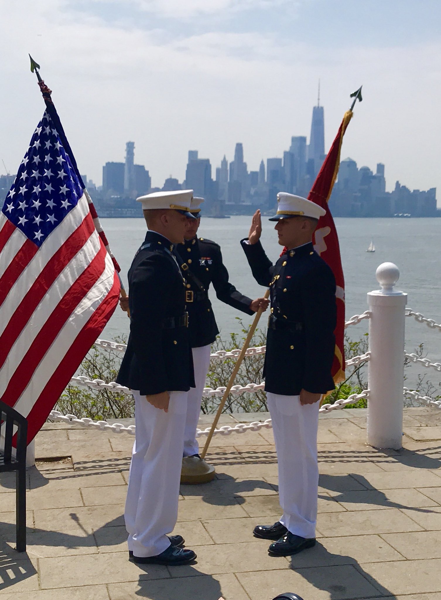 Two servicemen saluting with flags on waterfront