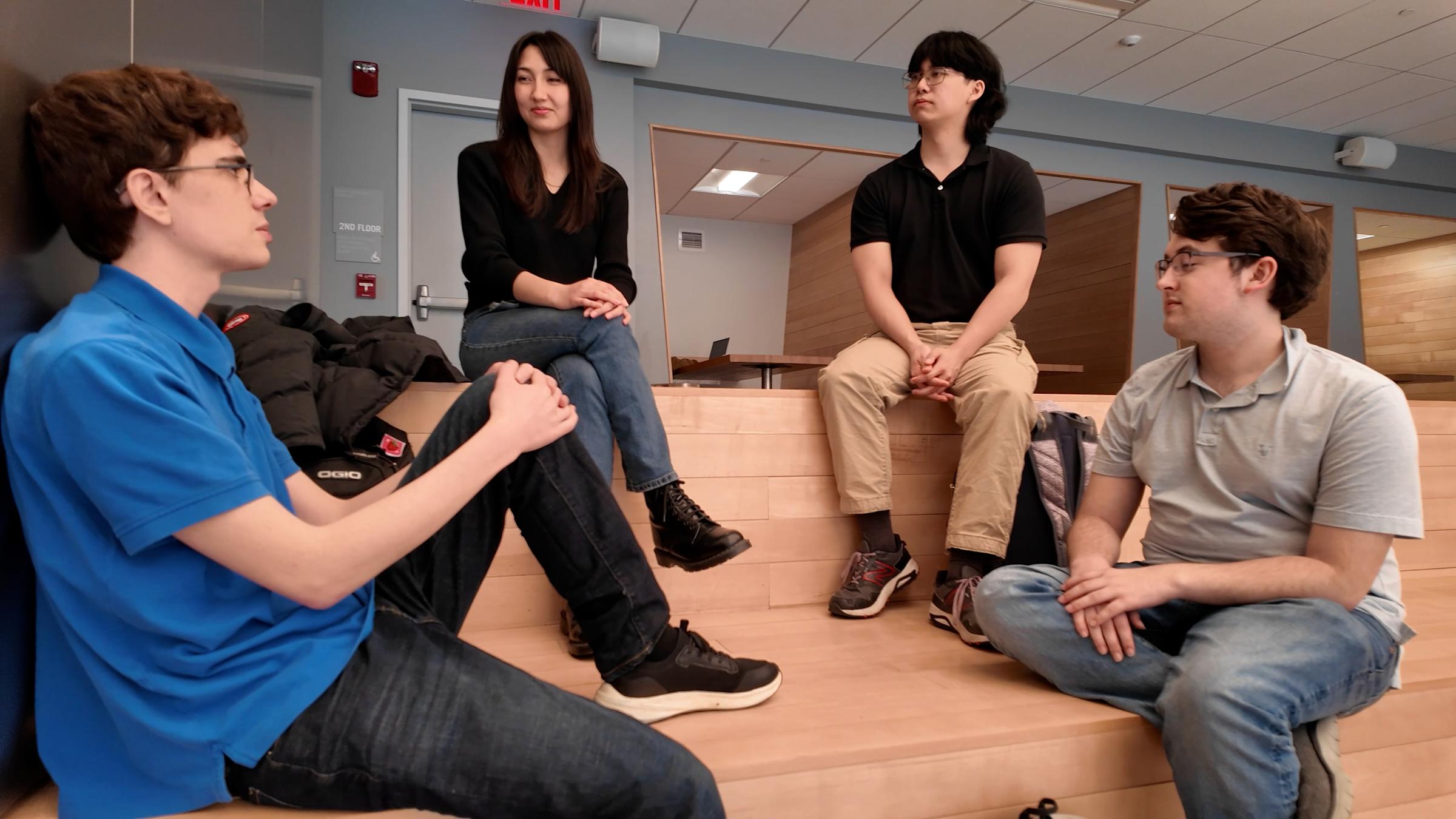 A group of four students sitting in a wooden sitting area having a discussion.