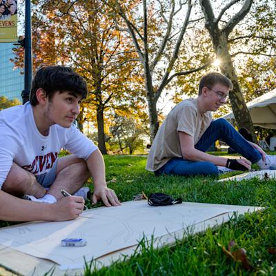 Two students outdors on campus drawing a building.