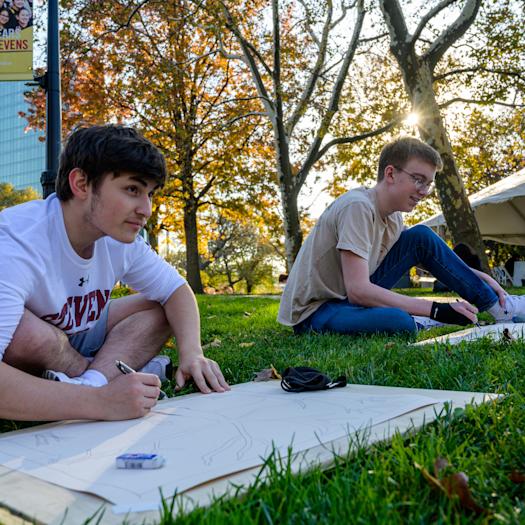 Two students outdors on campus drawing a building.