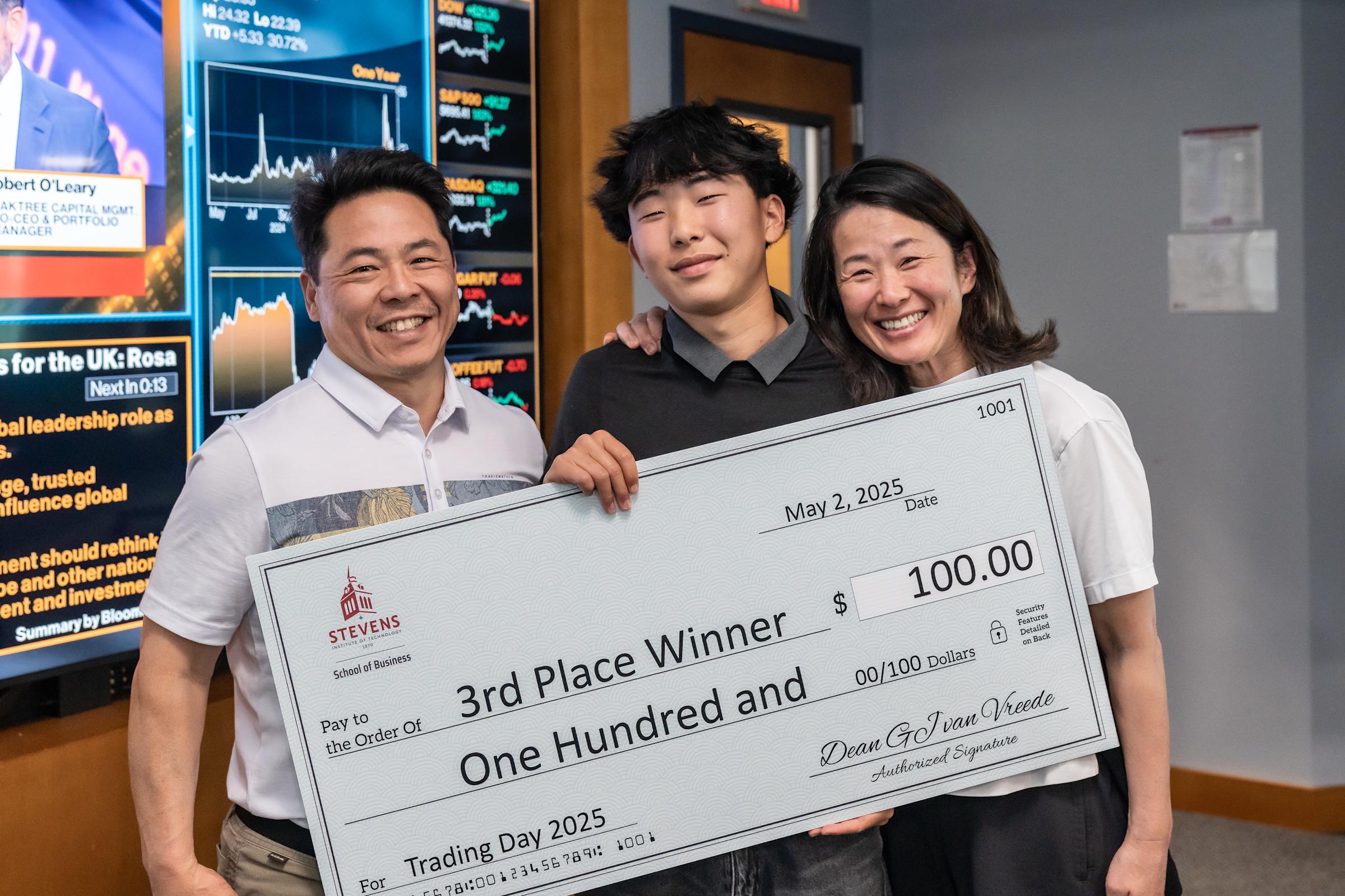 Third-place winner Reece Ho poses with his father and mother holding a giant check for $100.
