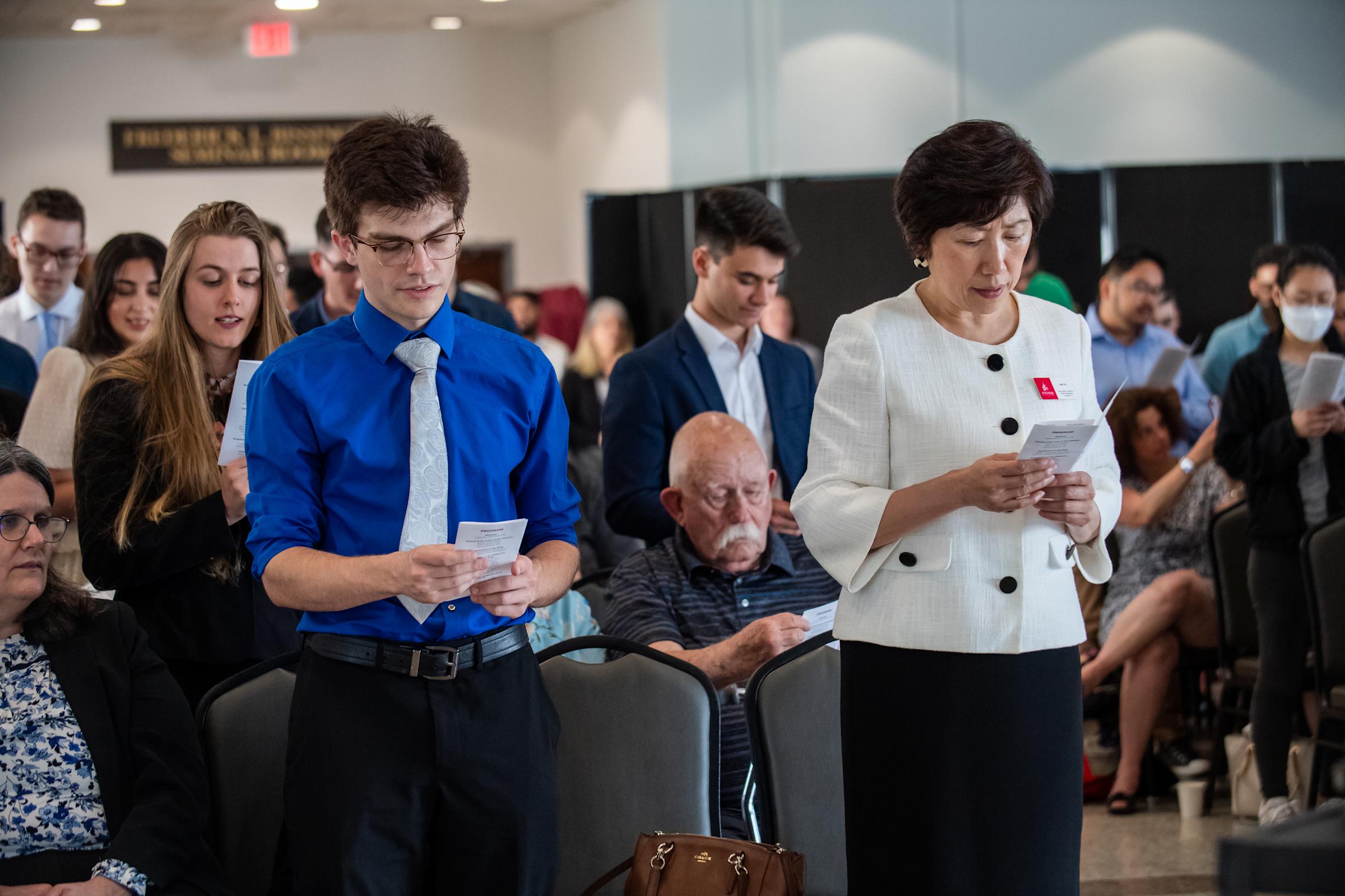 Students, professors, and Dean Zu standing, reading papers and reciting oath