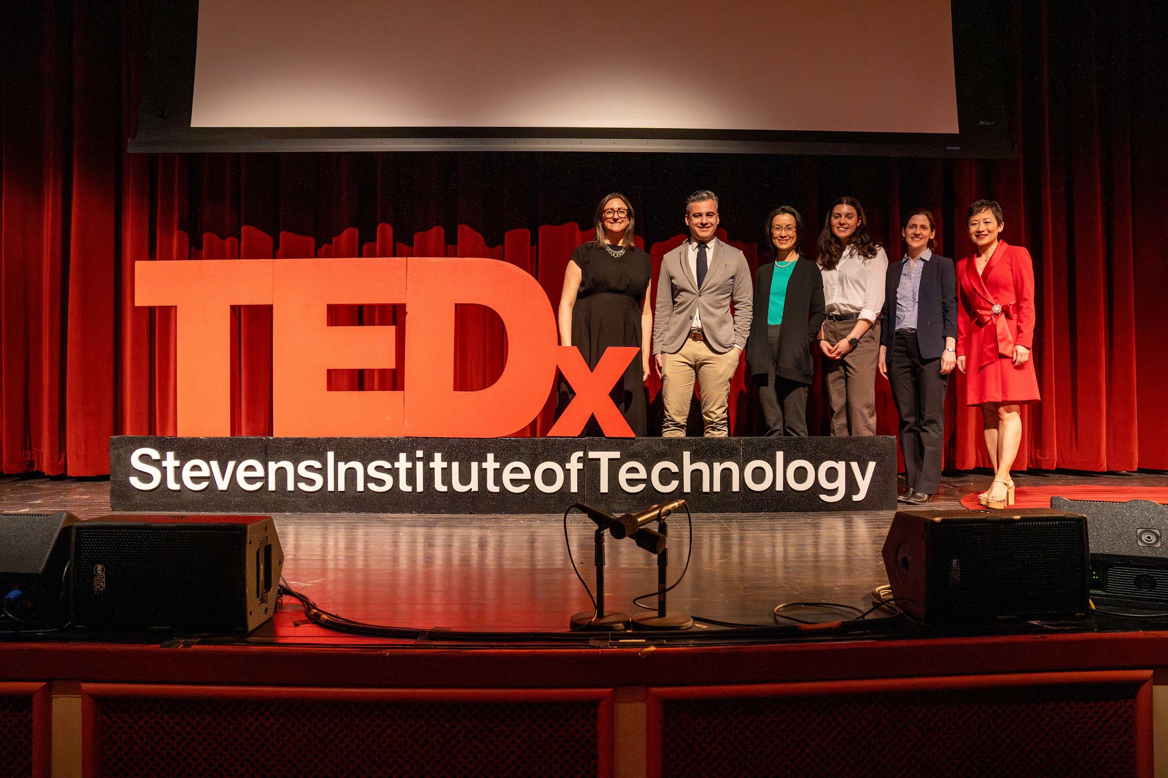 group of presenters pose for a photo together next to a TEDx and Stevens Institute of Technology sign