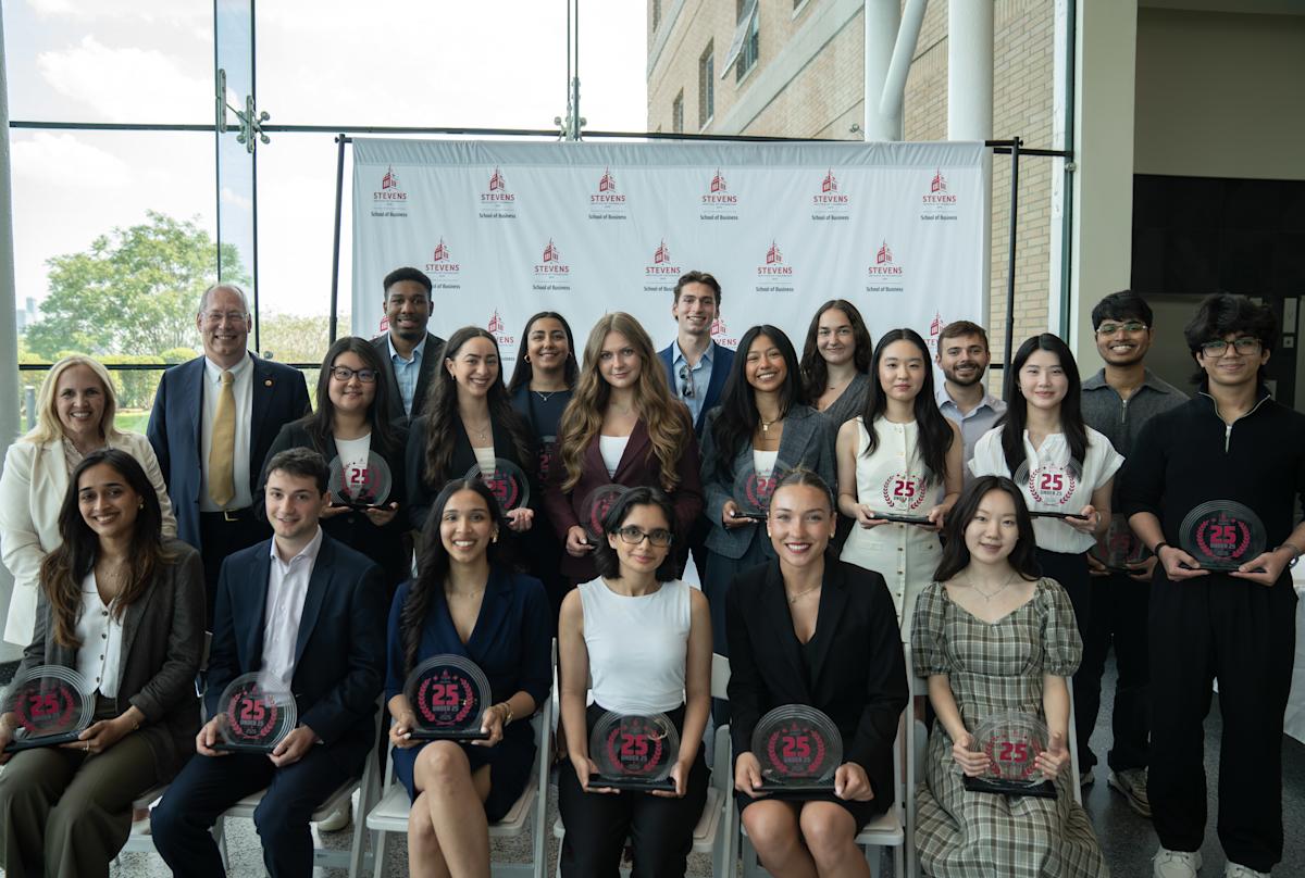 Inaugural 25 Under 25 cohort members pose for a group photo. They are dressed in business attire and are posed in front of a School of Business step and repeat banner