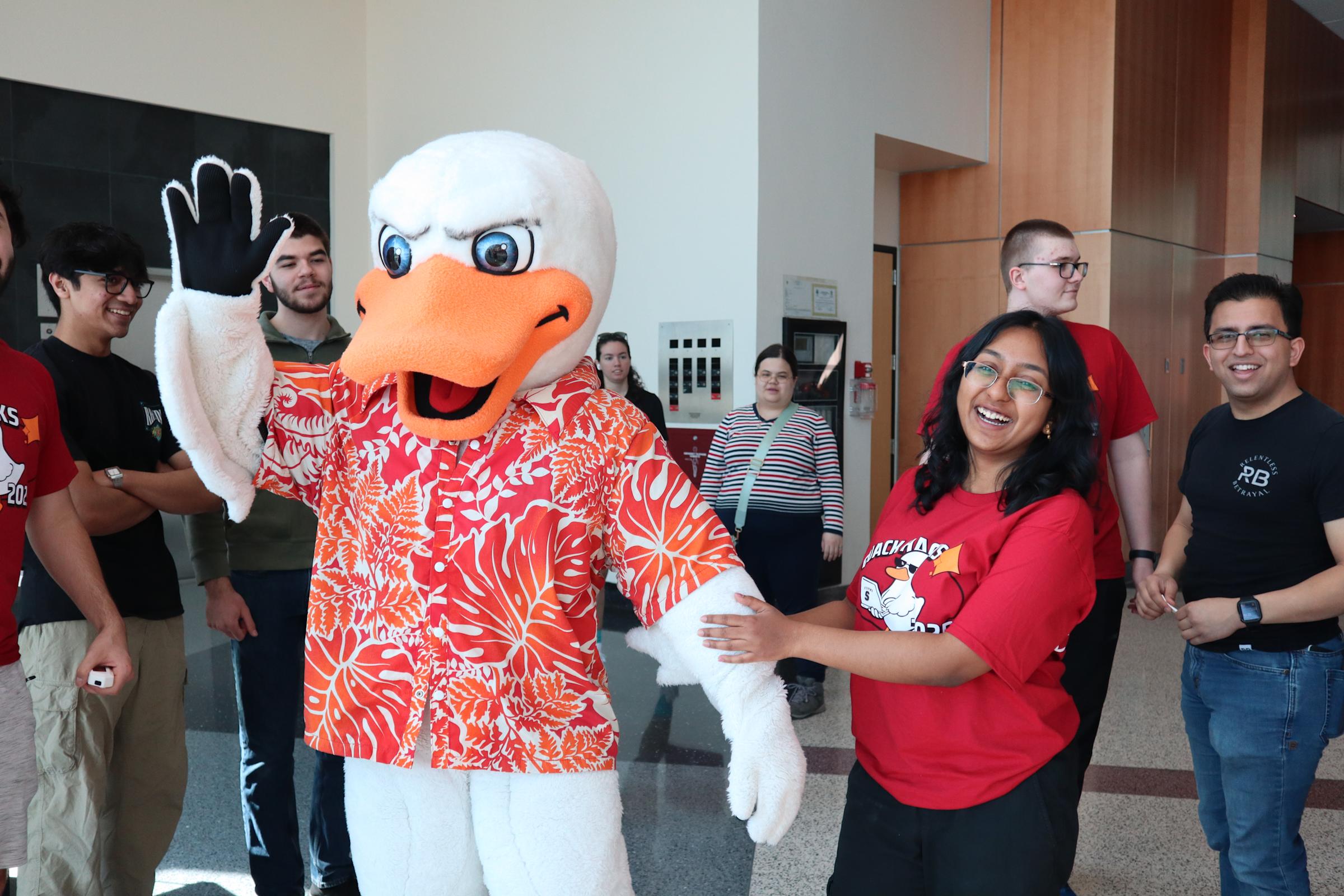 A student wearing a red Stevens shirt holds onto the arm of someone dressed up as the school mascot, Atilla the duck.