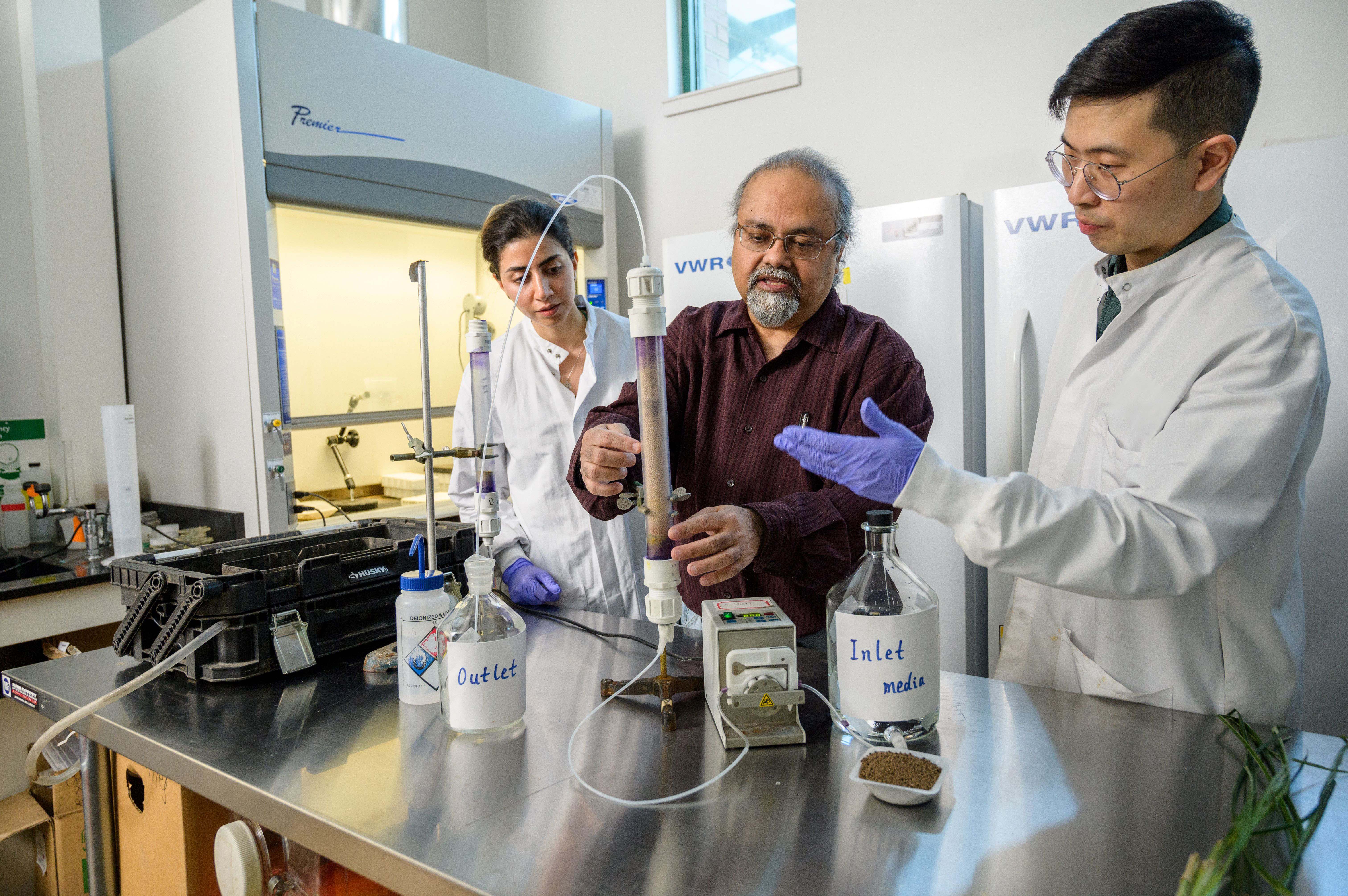 Stevens professor Dibs Sarkar is flanked by two students at a lab workstation with a test tube and glass bottles.