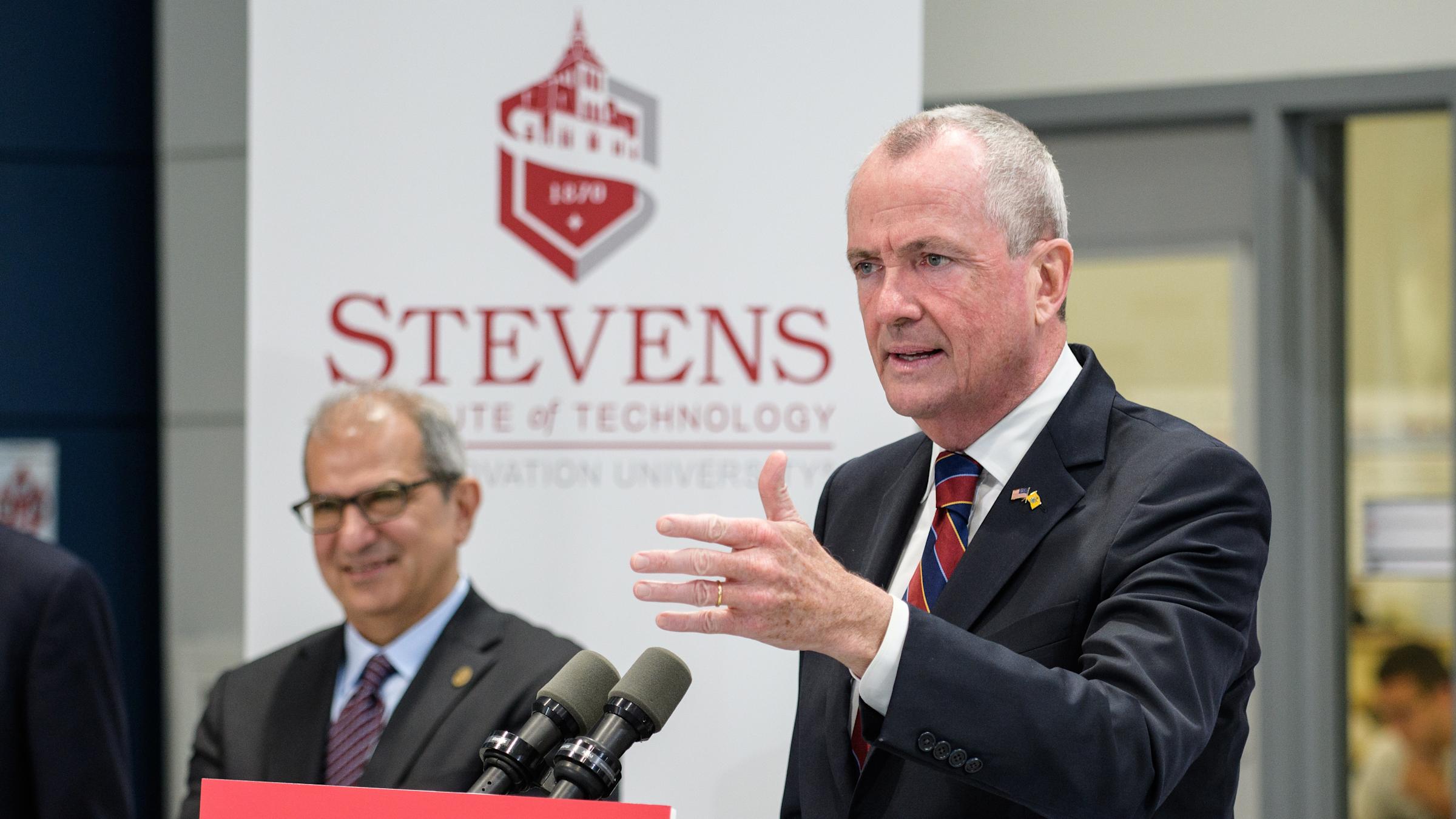 Gov. Phil Murphy speaking at the podium in the ABS Engineering Center at Stevens Institute of Technology as President Nariman Farvardin looks on