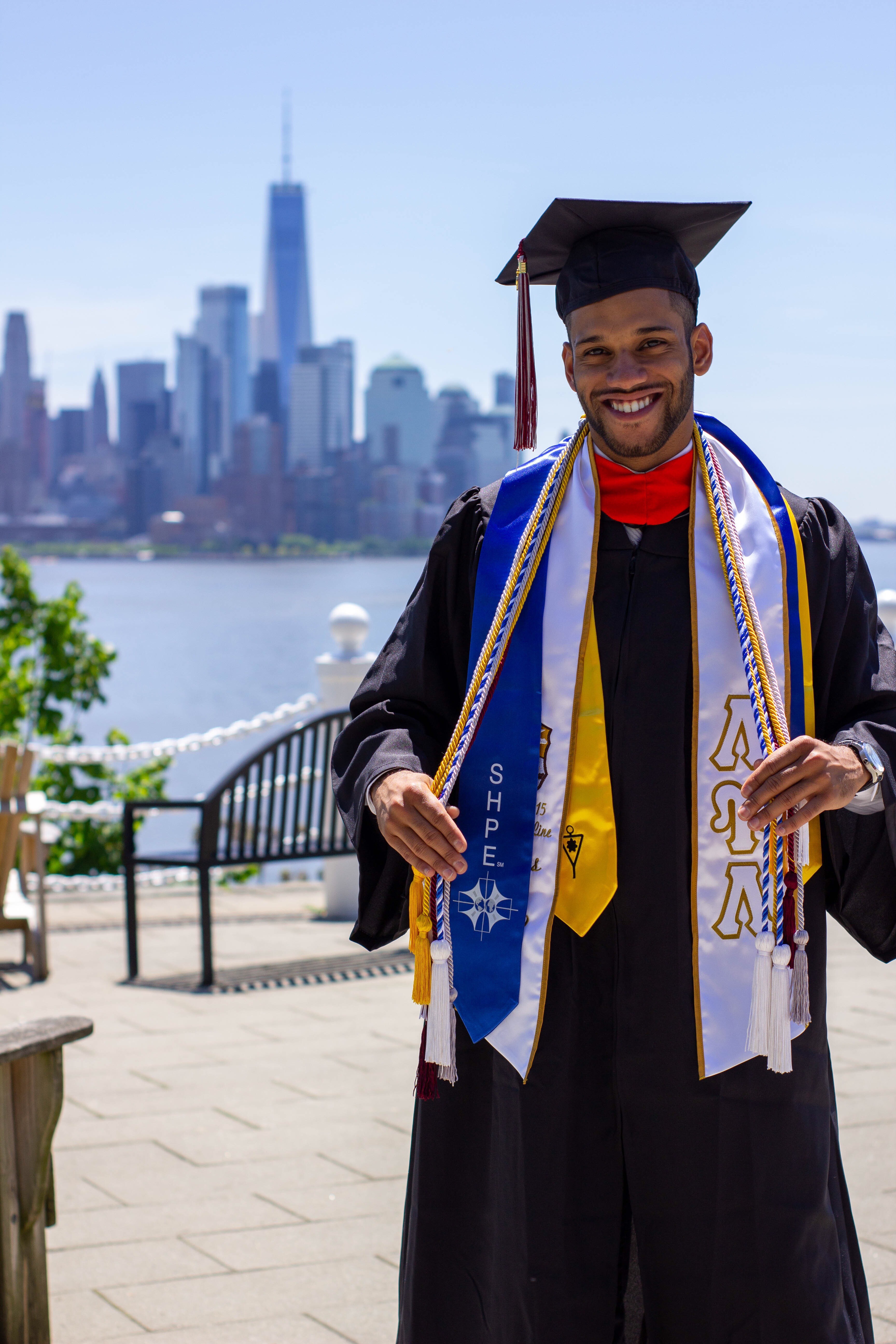 Jose Angeles-Ovalles, wearing his cap and gown, standing on Castle Point with Manhattan in the background on Commencement Day