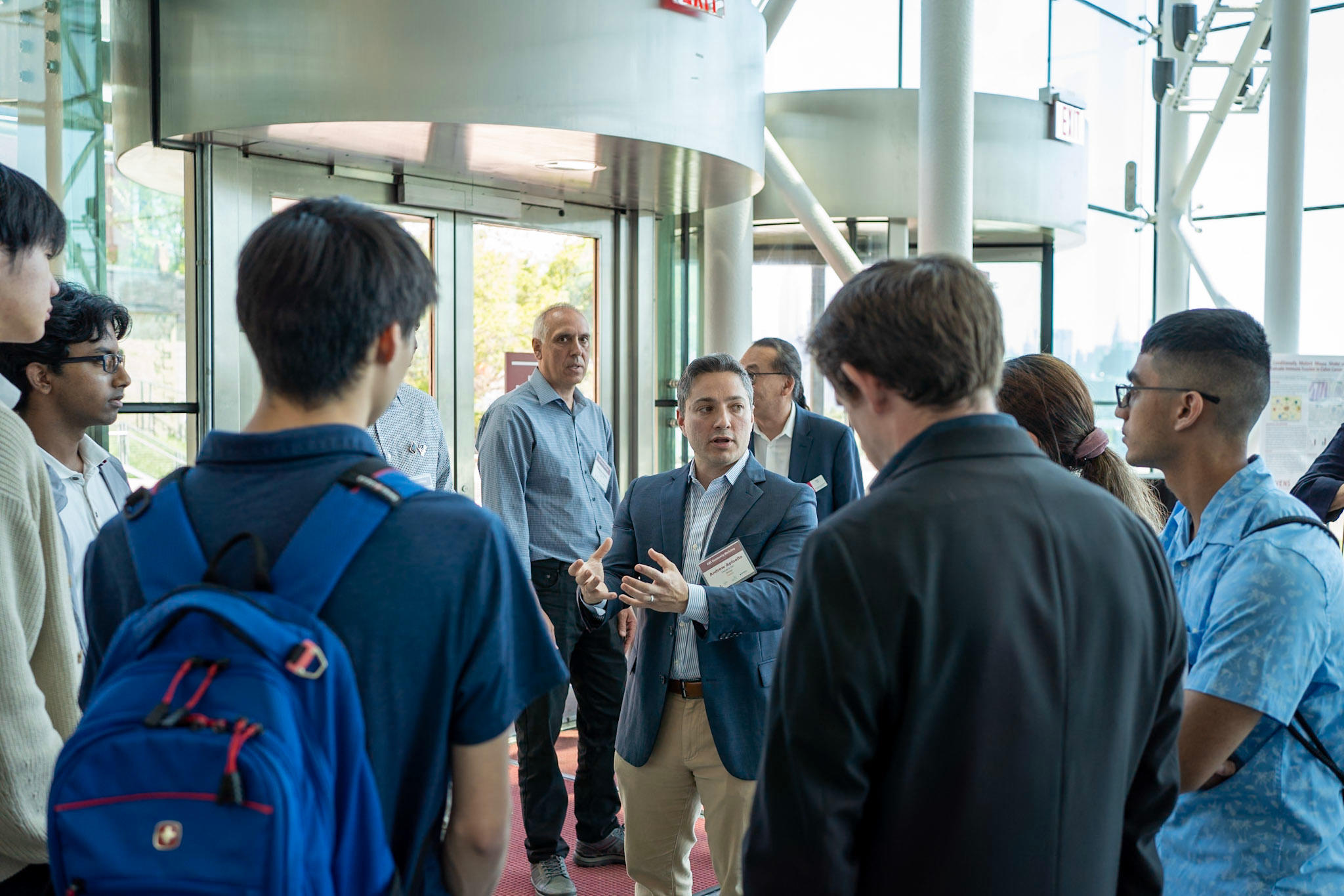 A group of students standing in a circle with an adult in the middle who is gesturing towards them and speaking with them.