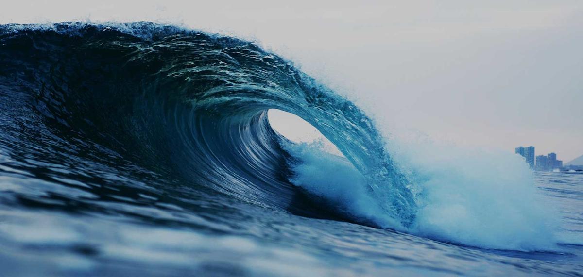 Rendering of a curling high wave in the ocean near a city in the background.