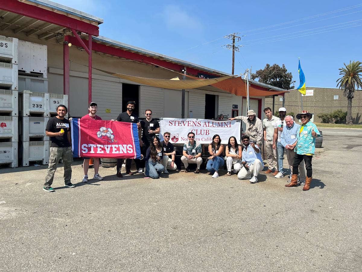 Members of the Northern California Regional Network gather at an event and pose with their Stevens Alumni Club banner and Stevens flag