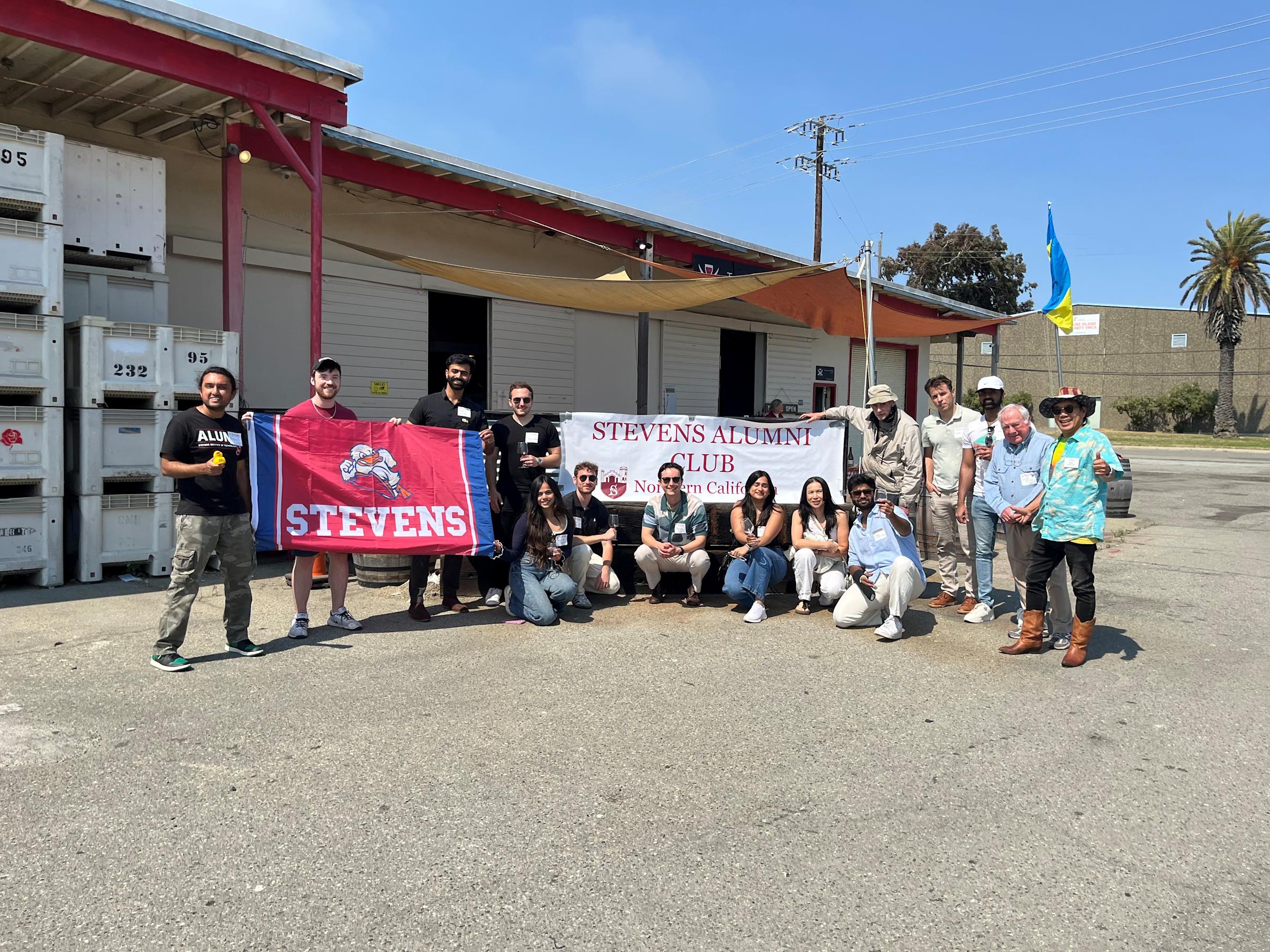 Members of the Northern California Regional Network gather at an event and pose with their Stevens Alumni Club banner and Stevens flag