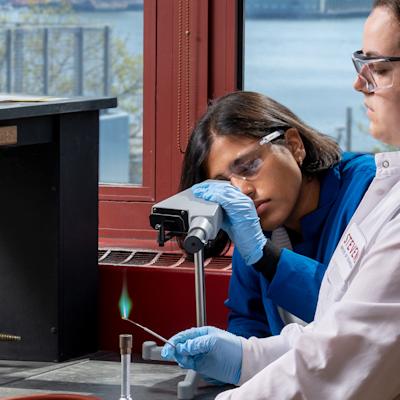 Two students in lab coats doing an experiment using a bunsen burner