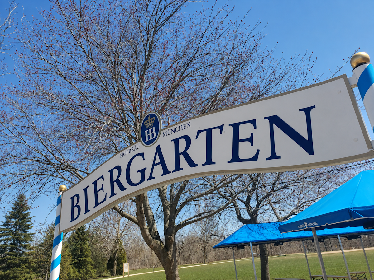 Blue and white sign outside against a blue sky, stating Hofbrau Munchen Biergarten