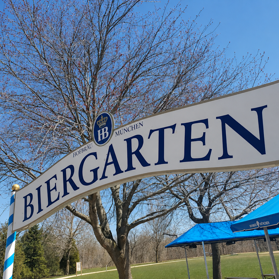 Blue and white sign outside against a blue sky, stating Hofbrau Munchen Biergarten