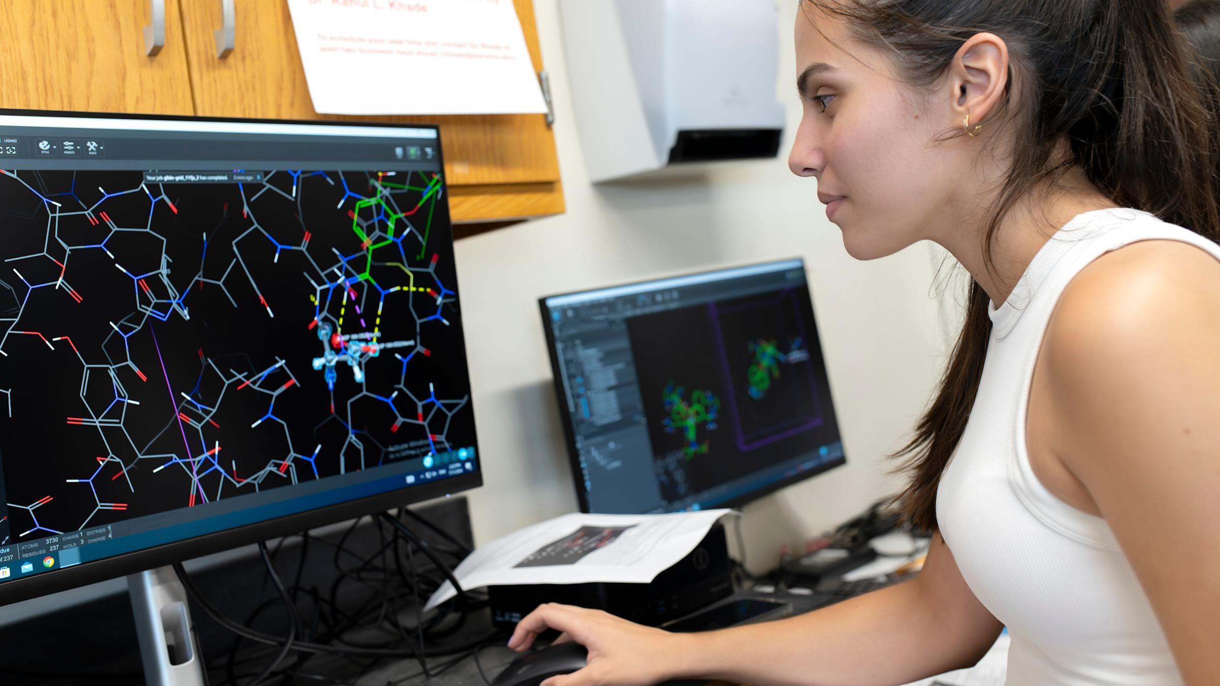 A student in a computer lab working on a program showing atomic structures.