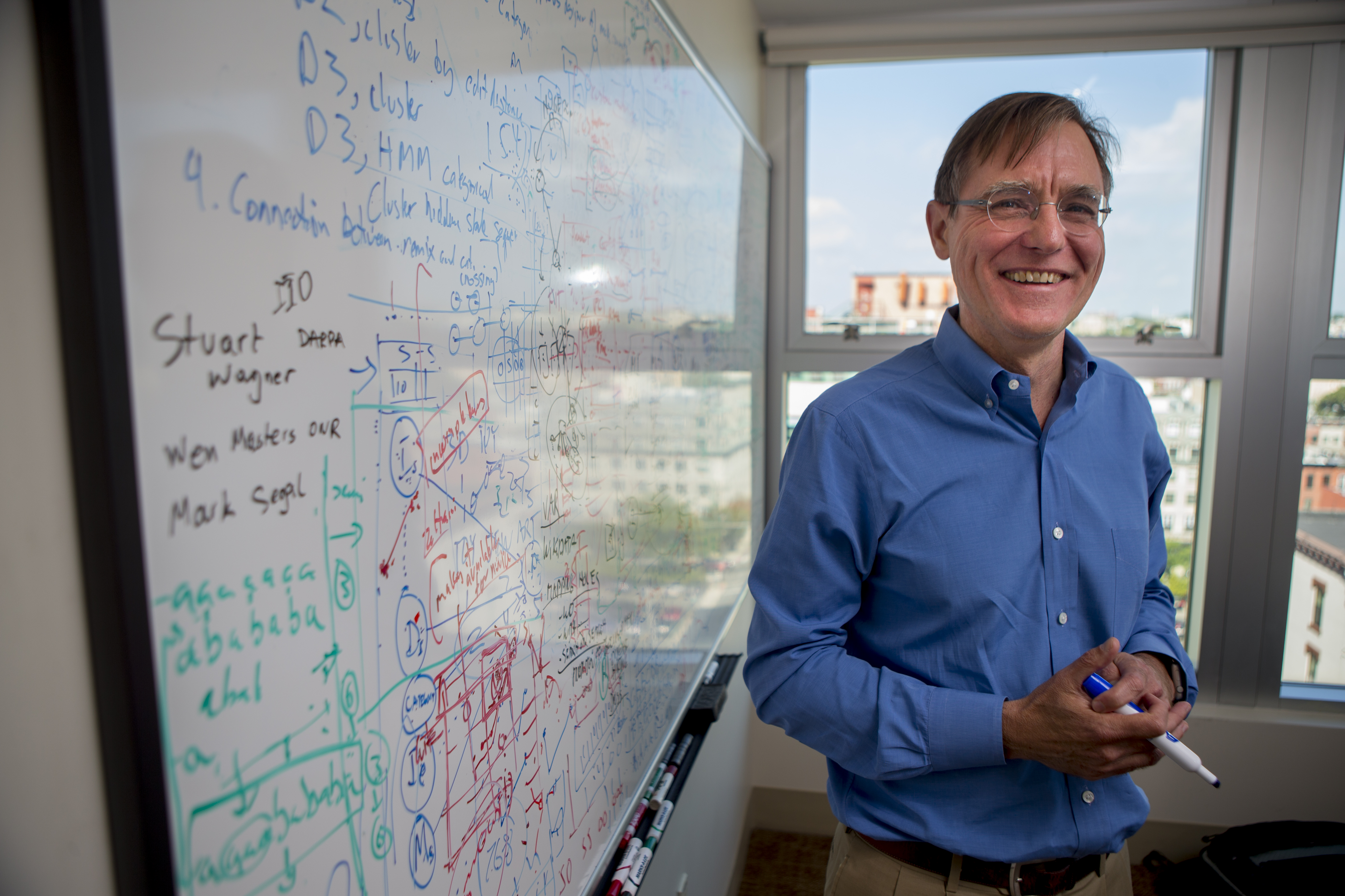Professor smiles and stands near whiteboard