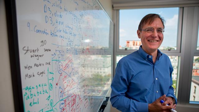 Professor smiles and stands near whiteboard