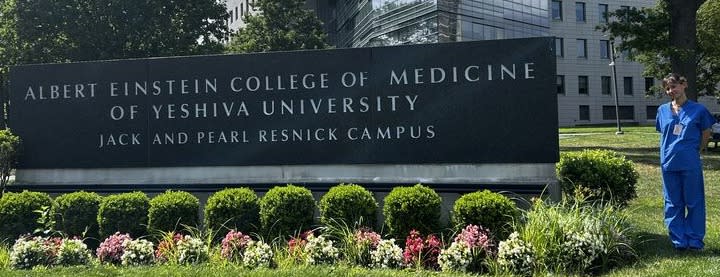 Chloe Borentain poses in a green field to the right of a sign that reads Albert Einstein College of Medicine of Yeshiva University Jack and Pearl Resnick Campus.