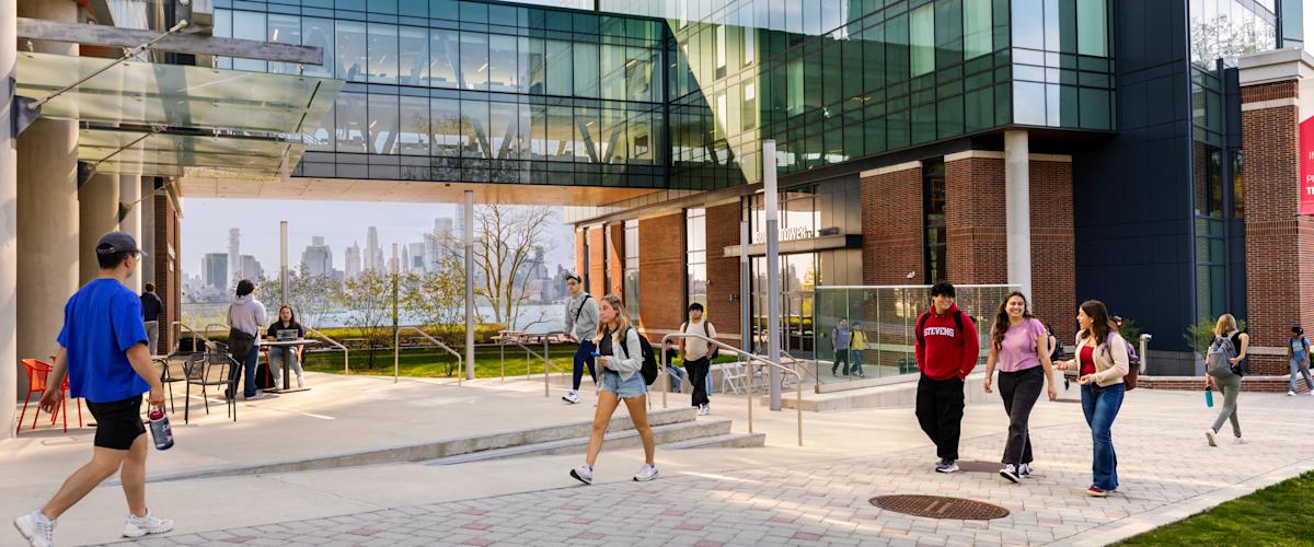 Students walk on a pathway upon Stevens campus with New York City skyline in the background.